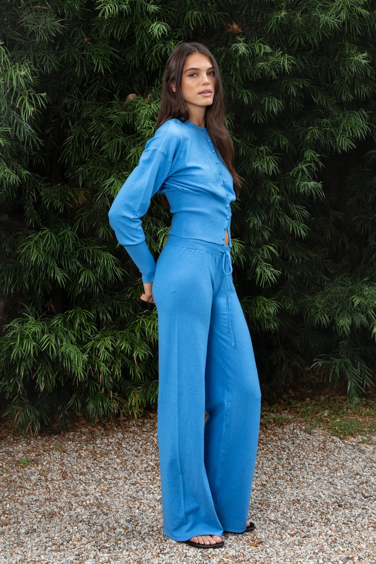 Woman wearing AZUREE button front cardigan and wide leg pants set featuring soft stretch sweater knit fabric, cropped cardigan with round neckline, covered button front closure, relaxed dropped shoulders, long sleeves with extended ribbed cuffs, fitted ribbed waistband, and matching high waisted pants with adjustable drawstring waist and relaxed full length wide leg silhouette.