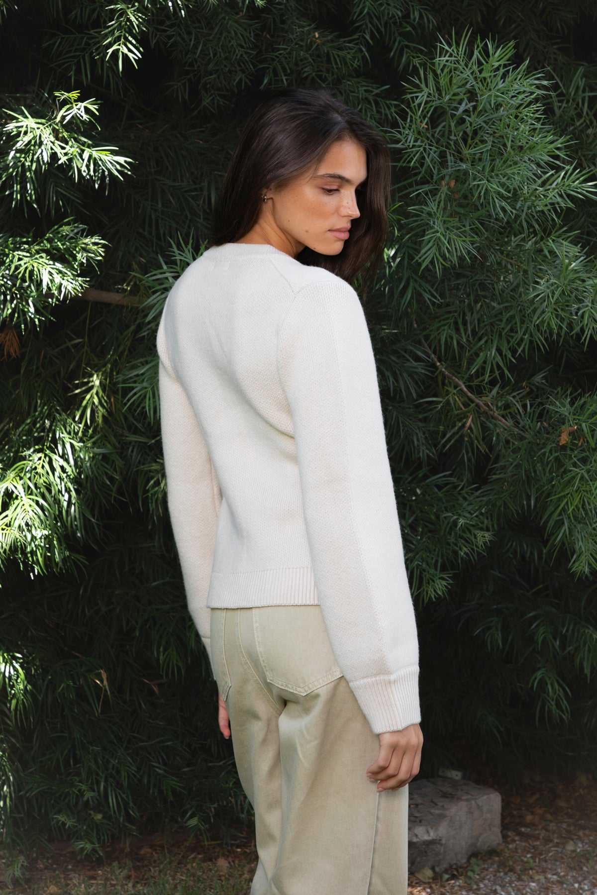 Woman wearing SABINE button front knit cardigan featuring soft textured sweater knit fabric with anti pilling finish, classic crew neckline with ribbed trim, full front closure with matching fabric covered buttons, long sleeves with ribbed cuffs, decorative front welt pockets, relaxed straight fit, slightly fitted waist, ribbed hem, and hip length silhouette.