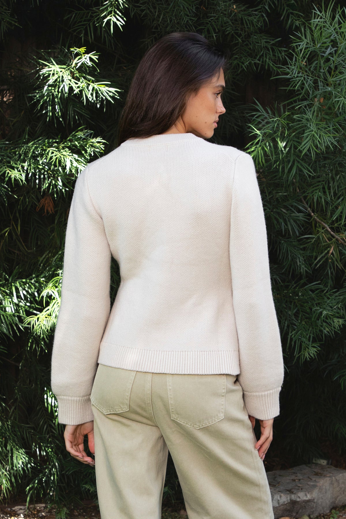 Woman wearing SABINE button front knit cardigan featuring soft textured sweater knit fabric with anti pilling finish, classic crew neckline with ribbed trim, full front closure with matching fabric covered buttons, long sleeves with ribbed cuffs, decorative front welt pockets, relaxed straight fit, slightly fitted waist, ribbed hem, and hip length silhouette.