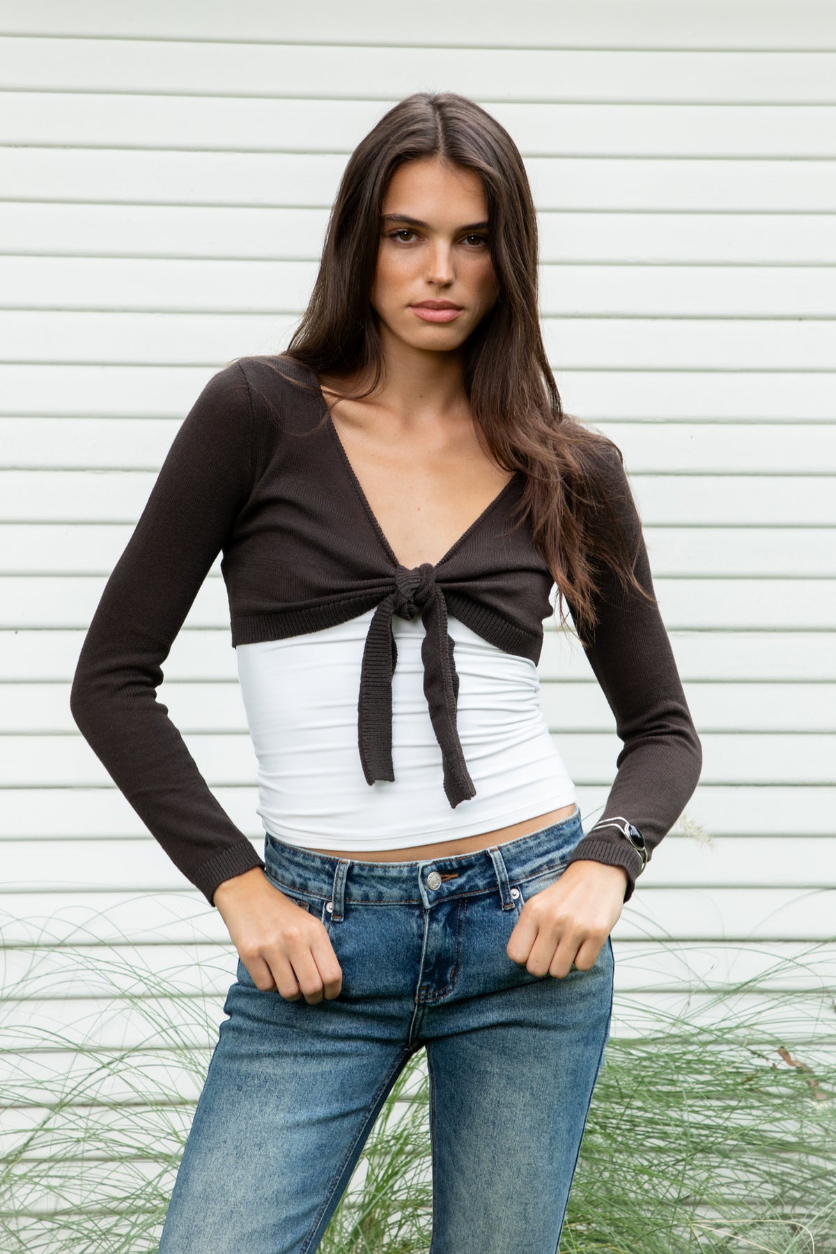 Woman wearing LUCIENNE front tie cropped bolero cardigan featuring soft lightweight cotton sweater knit fabric, deep V neckline, open front design, adjustable front tie closure at the bust, ultra cropped bolero silhouette, long fitted sleeves with ribbed cuffs, delicate knit trim along the neckline, and ribbed hem for a clean fitted finish.