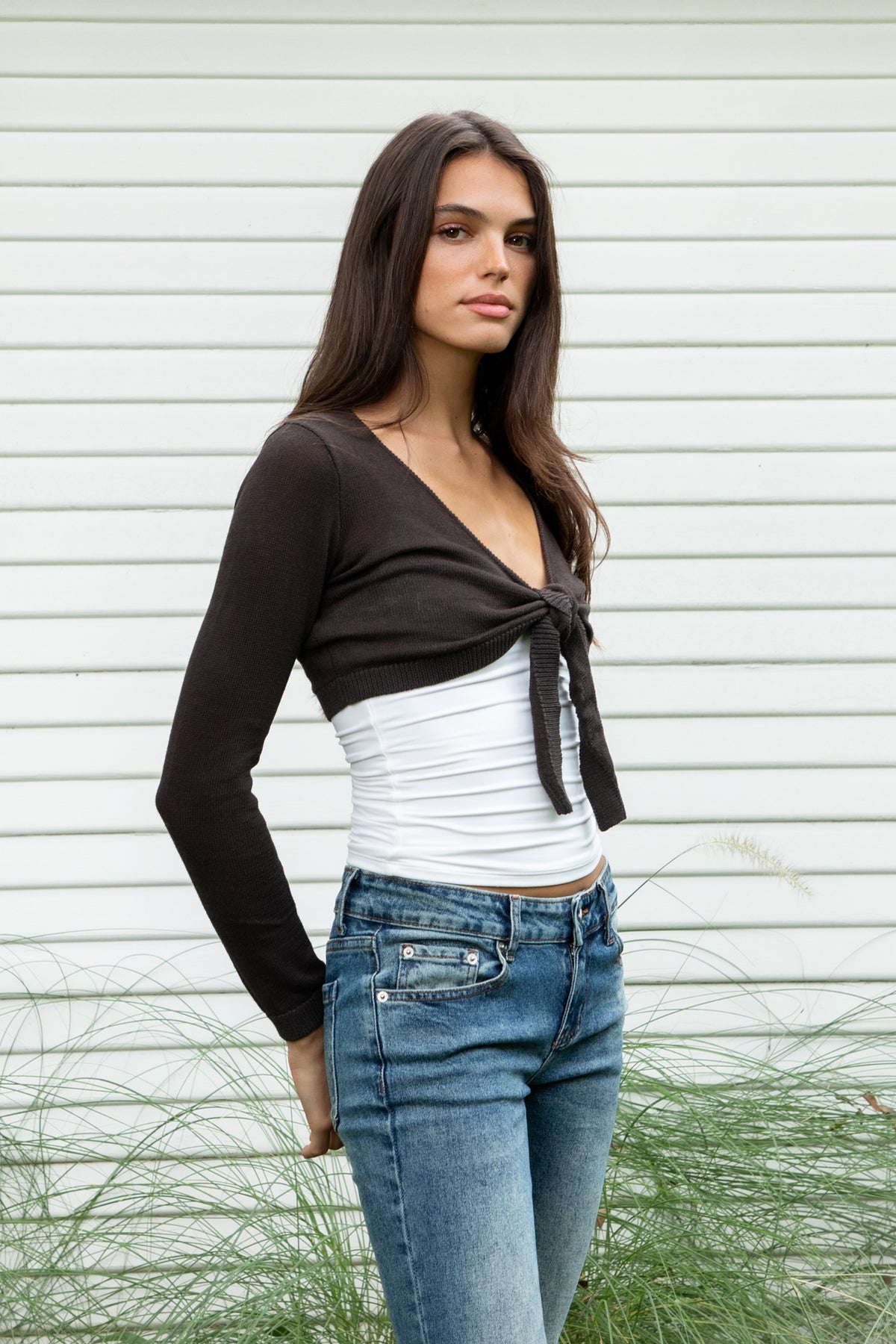 Woman wearing LUCIENNE front tie cropped bolero cardigan featuring soft lightweight cotton sweater knit fabric, deep V neckline, open front design, adjustable front tie closure at the bust, ultra cropped bolero silhouette, long fitted sleeves with ribbed cuffs, delicate knit trim along the neckline, and ribbed hem for a clean fitted finish.