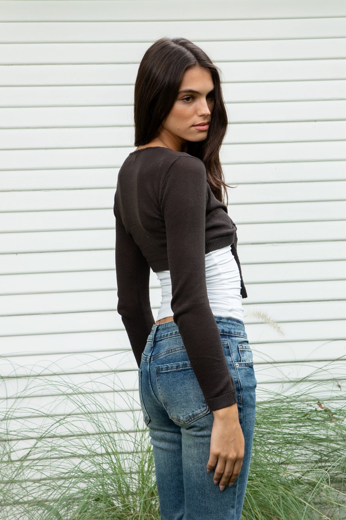 Woman wearing LUCIENNE front tie cropped bolero cardigan featuring soft lightweight cotton sweater knit fabric, deep V neckline, open front design, adjustable front tie closure at the bust, ultra cropped bolero silhouette, long fitted sleeves with ribbed cuffs, delicate knit trim along the neckline, and ribbed hem for a clean fitted finish.