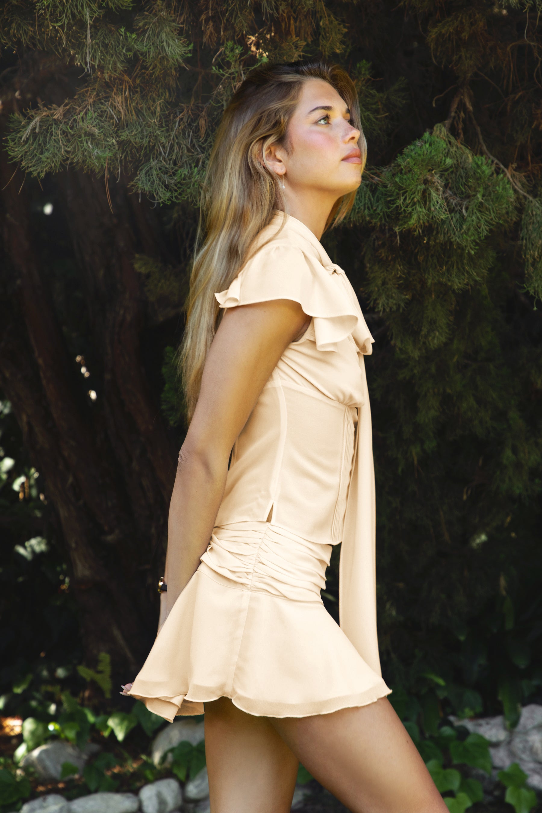 Woman wearing ROSELLIA pearl chiffon blouse and skirt set featuring a lightweight chiffon fabric, scarf detail with flowing drape, flutter sleeves, keyhole front with button closure and pleated bodice, and a low-rise mini skirt with ruched waist, concealed zipper, and stretch satin lining.