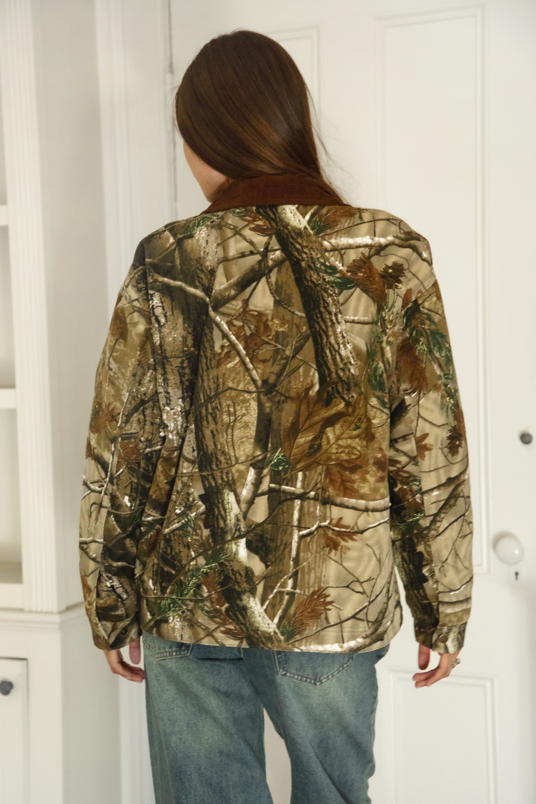 Woman wearing TIC TOC TT31858-LAUREL LAUREL oversized corduroy collar camo jacket featuring an allover wild camo print canvas twill body, contrast corduroy collar, front zipper closure, front two pockets, drop shoulder oversized fit, and satin quilted lining, styled with denim and a simple top for a western streetwear-inspired everyday look.