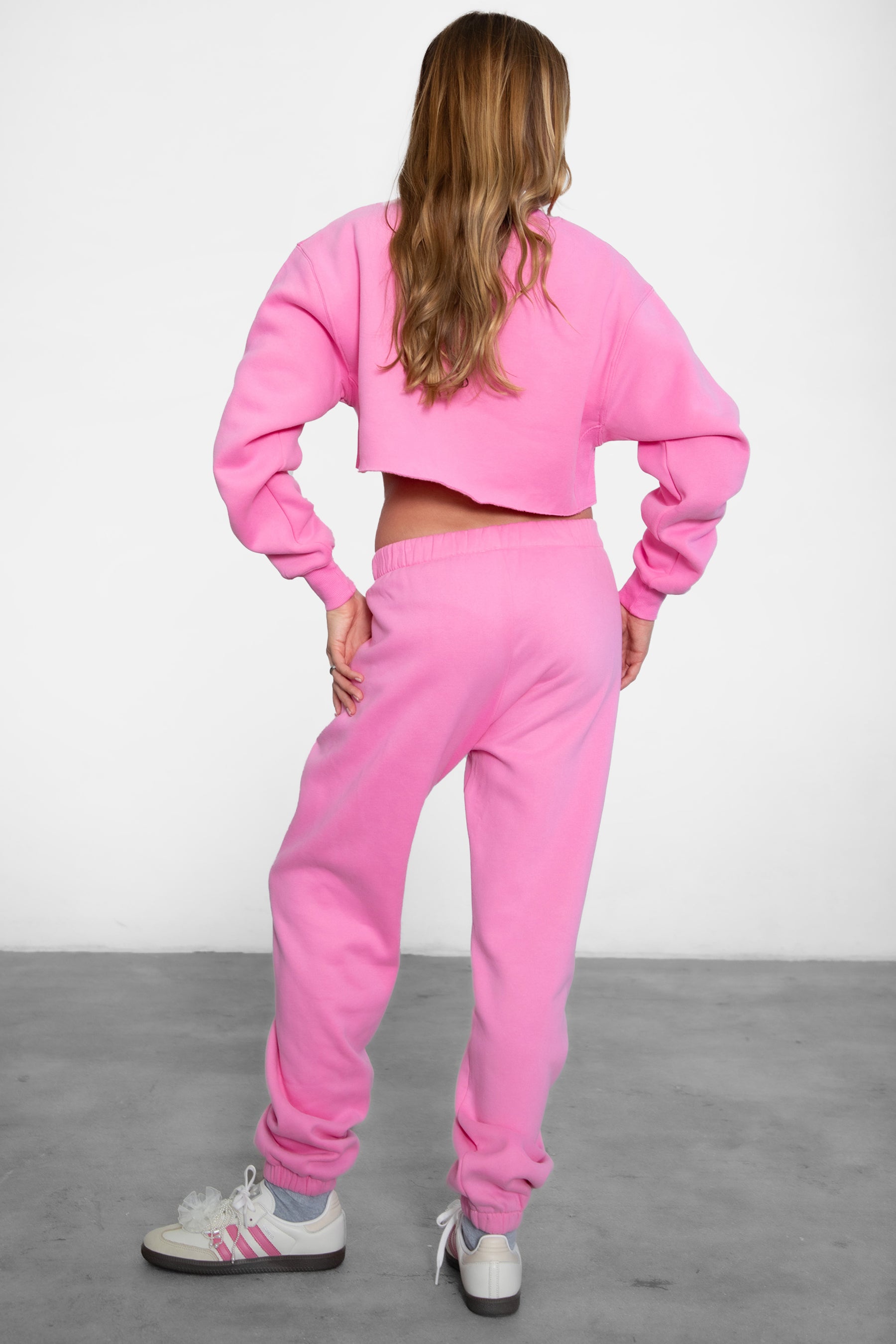 A person wearing high-waisted bright pink sweatpants with an elastic waistband and side pockets, paired with a matching top. 