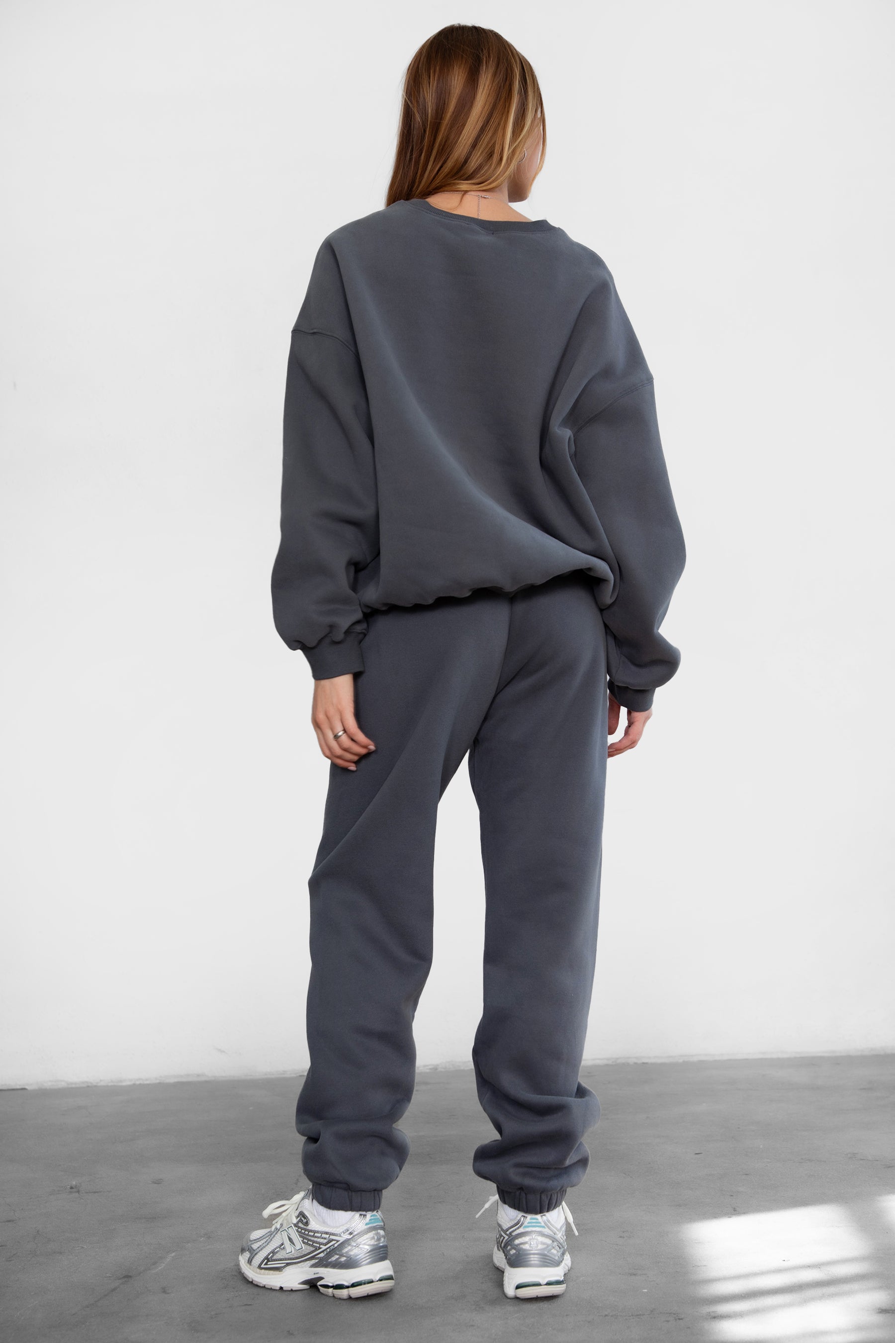 Woman wearing the TIC TOC PH26027 DOVE graphite high waist sweatpants featuring an elastic waistband, deep side pockets, and tapered ankle hem with a matching top. 