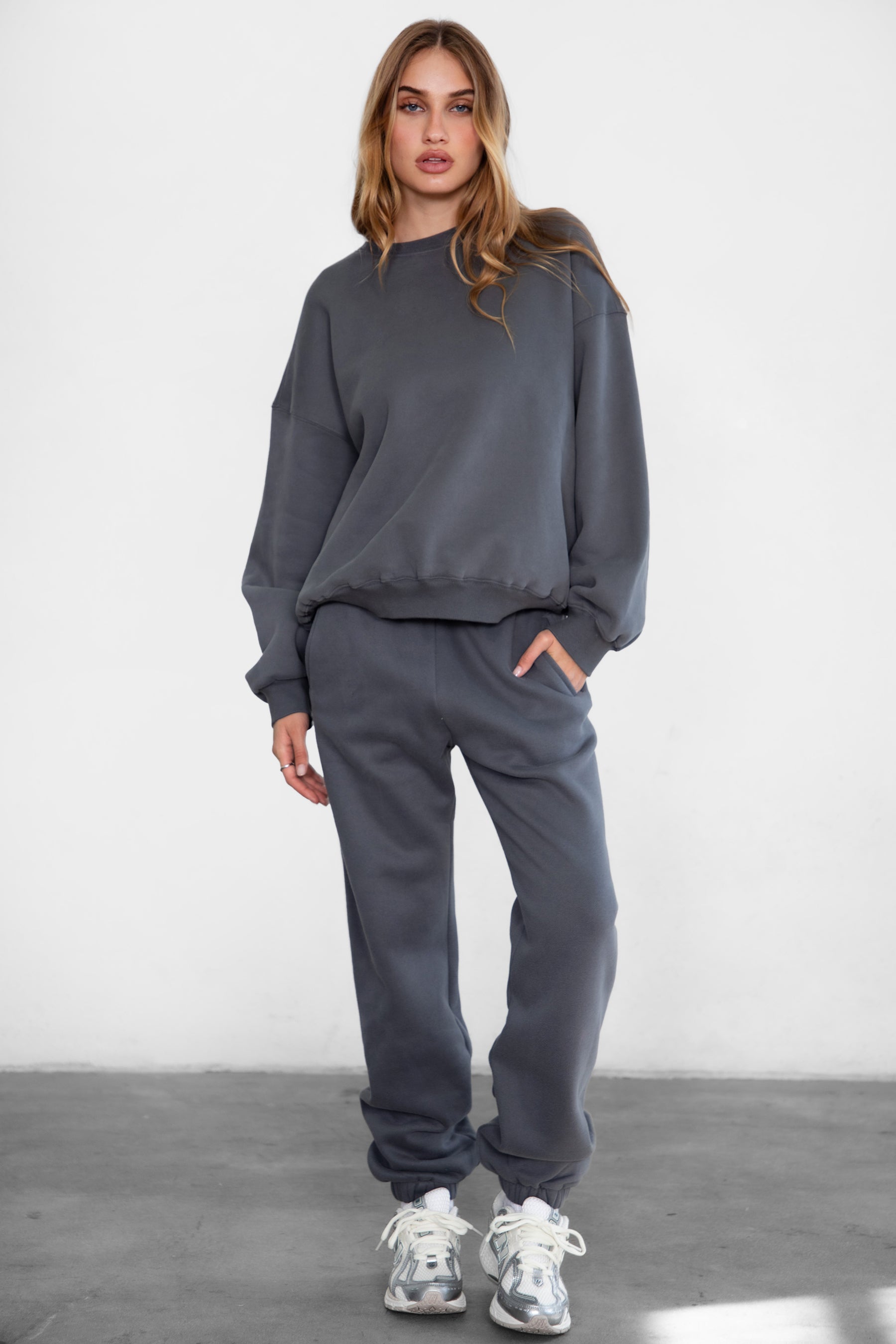 Woman wearing the TIC TOC PH26027 DOVE graphite high waist sweatpants featuring an elastic waistband, deep side pockets, and tapered ankle hem with a matching top. 