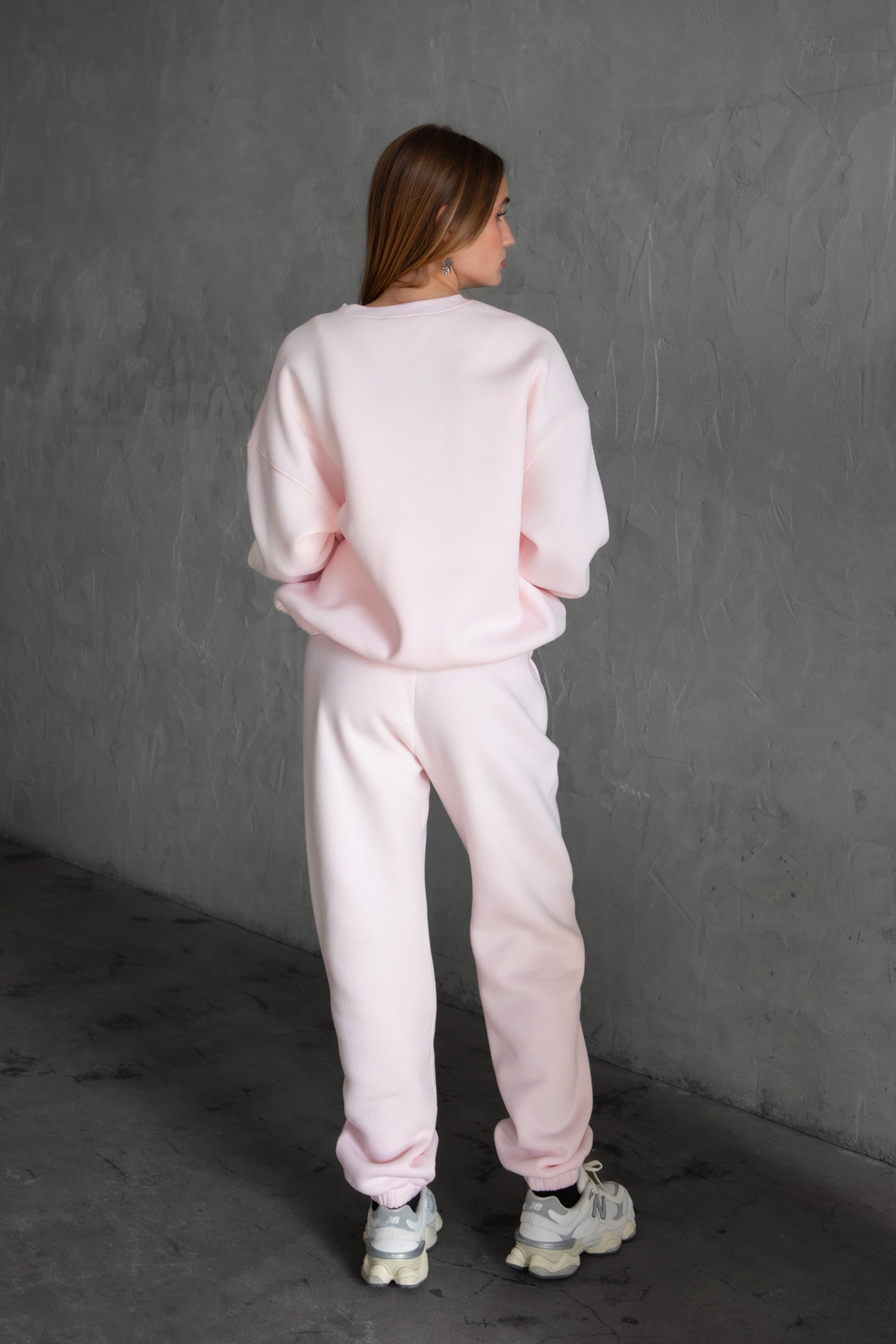 A person wearing high-waisted pink sweatpants with an elastic waistband and side pockets, paired with white sneakers.