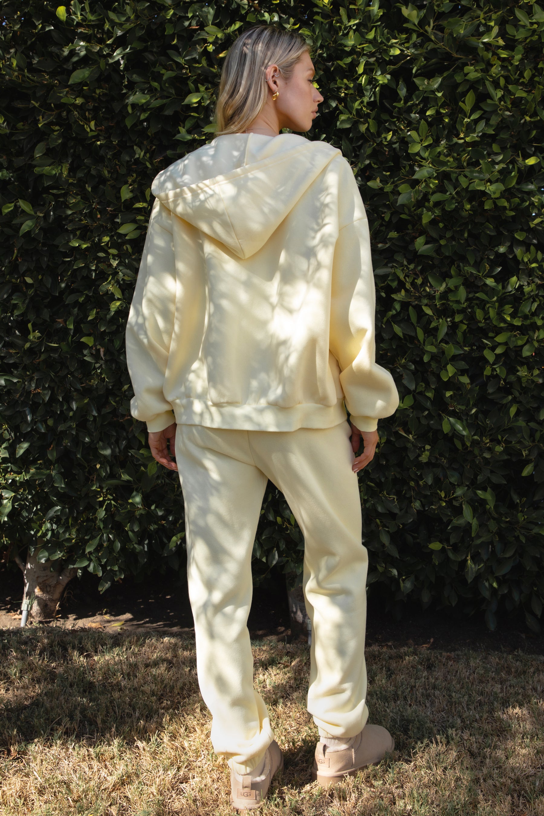 Woman wearing the TIC TOC PH26027 DOVE pale yellow high waist sweatpants featuring an elastic waistband, deep side pockets, and tapered ankle hem with a matching top. 