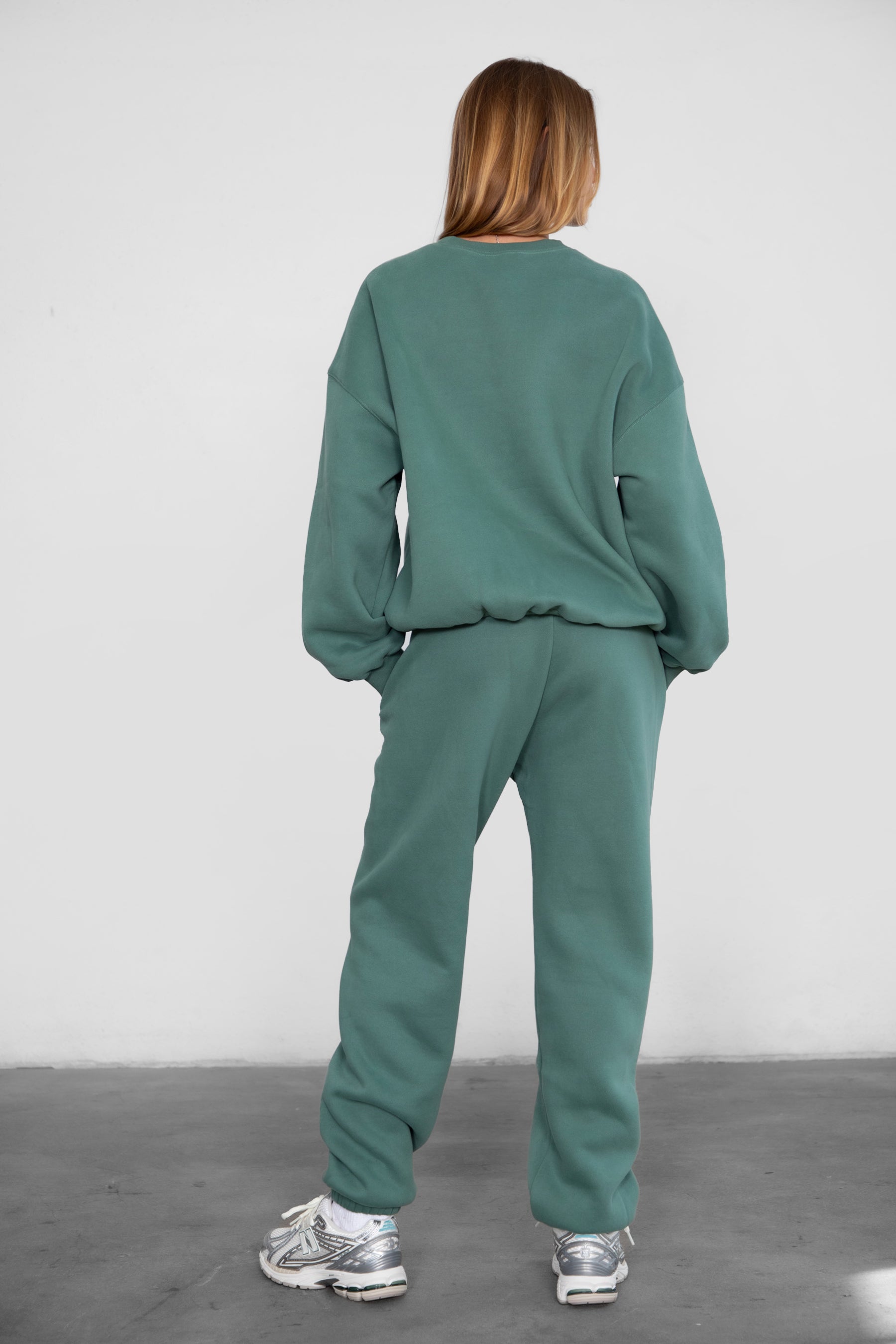 Woman wearing the TIC TOC PH26027 DOVE pine green high waist sweatpants featuring an elastic waistband, deep side pockets, and tapered ankle hem with a matching top. 