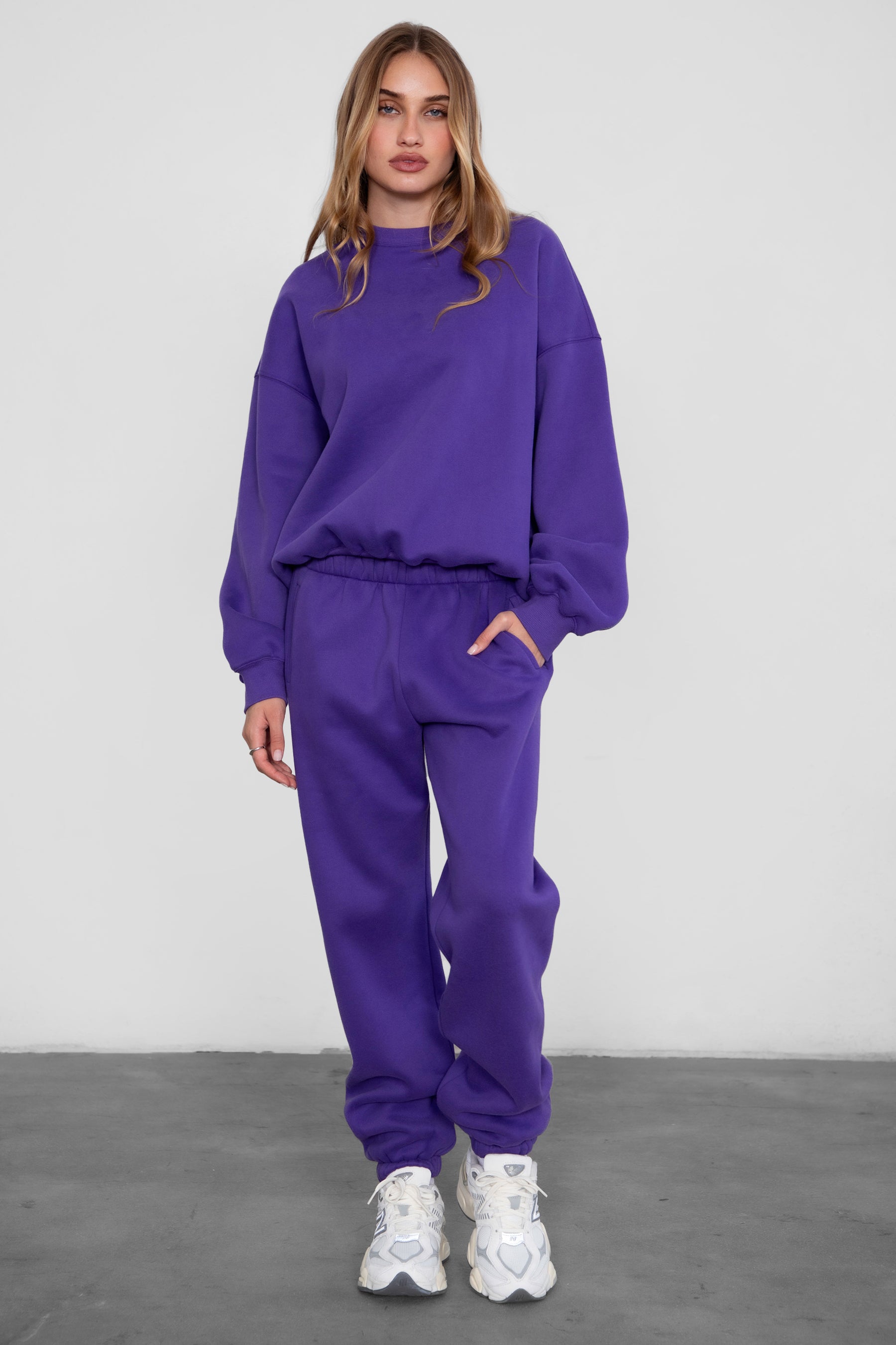 Woman wearing the TIC TOC PH26027 DOVE purple high waist sweatpants featuring an elastic waistband, deep side pockets, and tapered ankle hem with a matching top. 