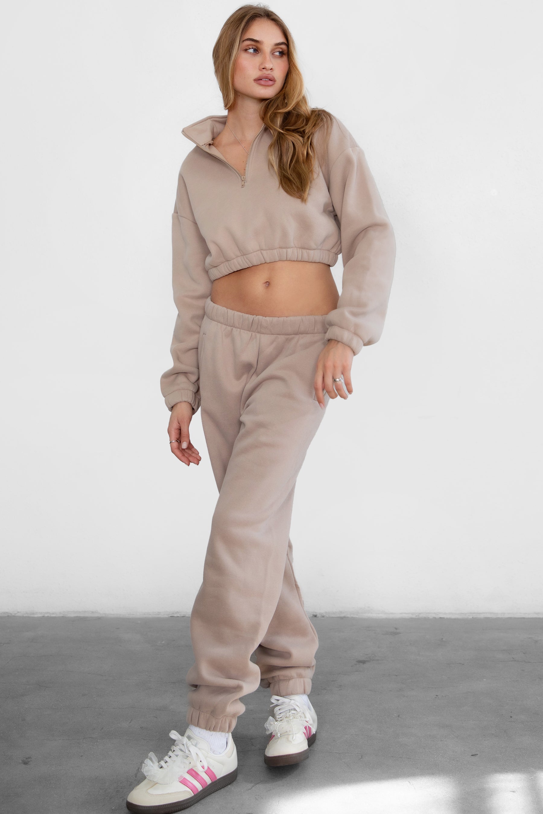 Woman wearing the TIC TOC PH26027 DOVE taupe high waist sweatpants featuring an elastic waistband, deep side pockets, and tapered ankle hem with a matching top. 