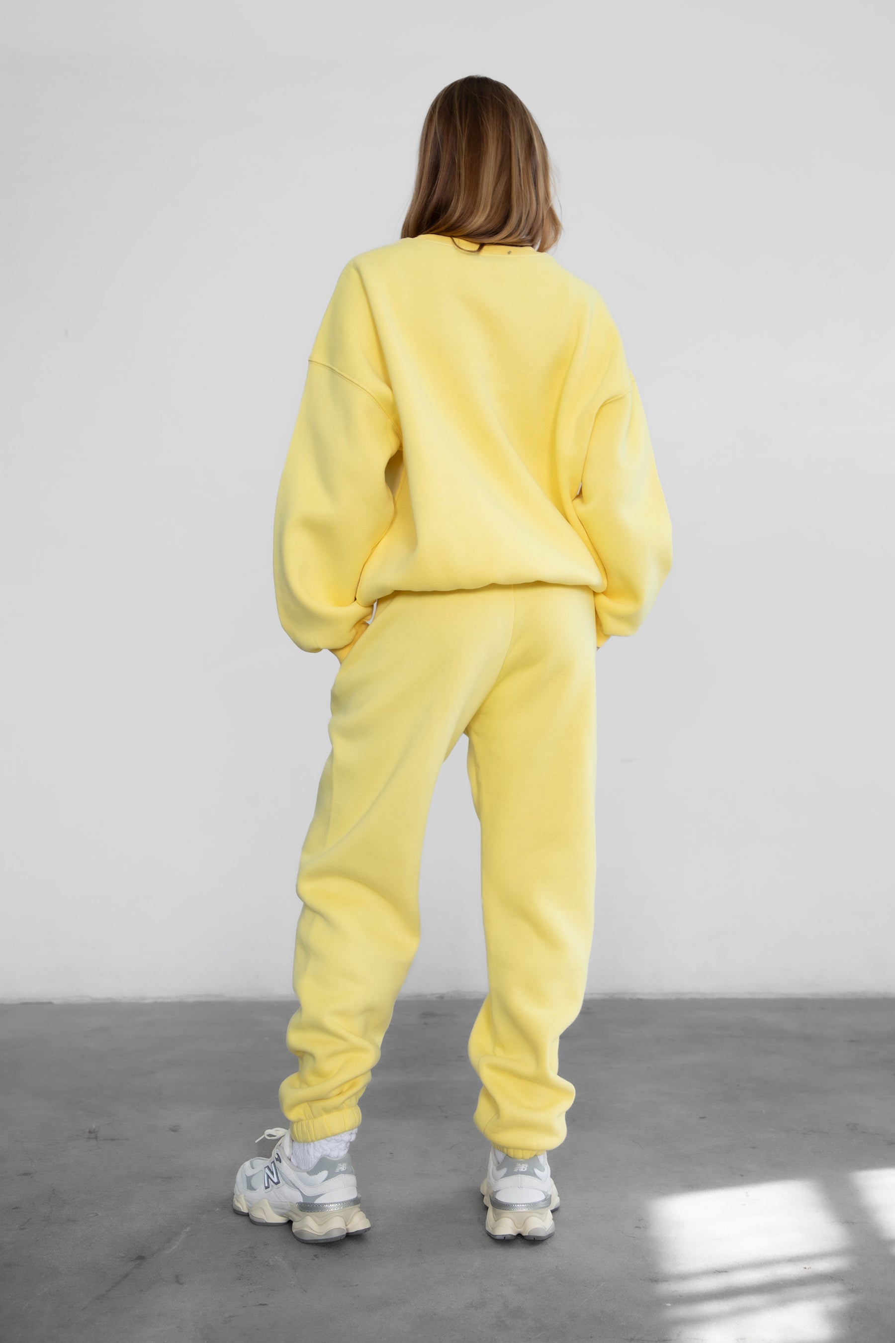 Woman wearing the TIC TOC PH26027 DOVE yellow high waist sweatpants featuring an elastic waistband, deep side pockets, and tapered ankle hem with a matching top. 