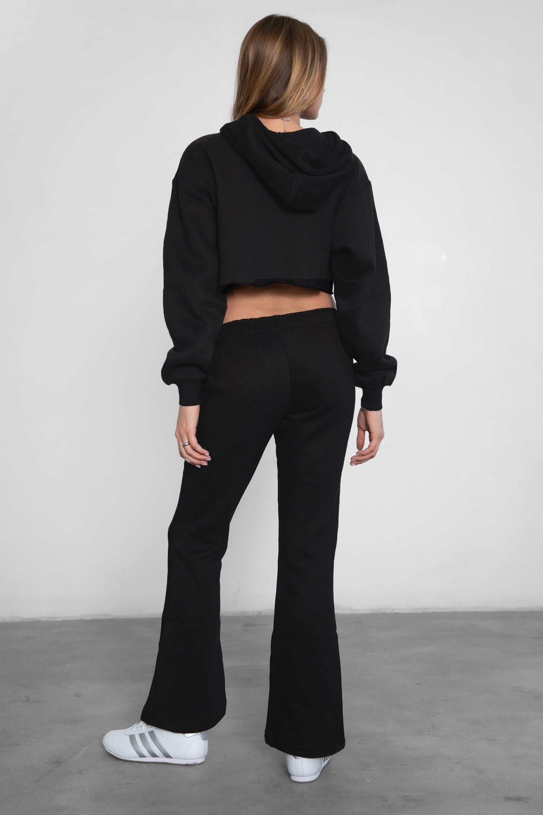 Woman wearing TIC TOC PH29142 JIYA essential fleece flare sweatpants with mid-rise waistband and side pockets from plush fleece collection  in black paired with a raw cut matching hoodie. 