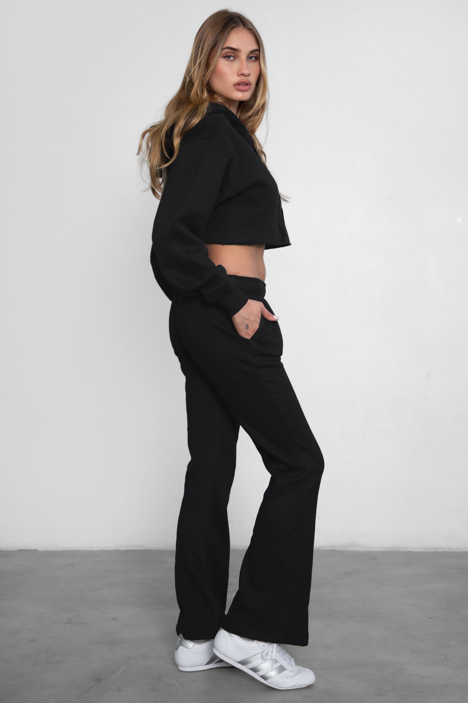 Woman wearing TIC TOC PH29142 JIYA essential fleece flare sweatpants with mid-rise waistband and side pockets from plush fleece collection  in black paired with a raw cut matching hoodie. 
