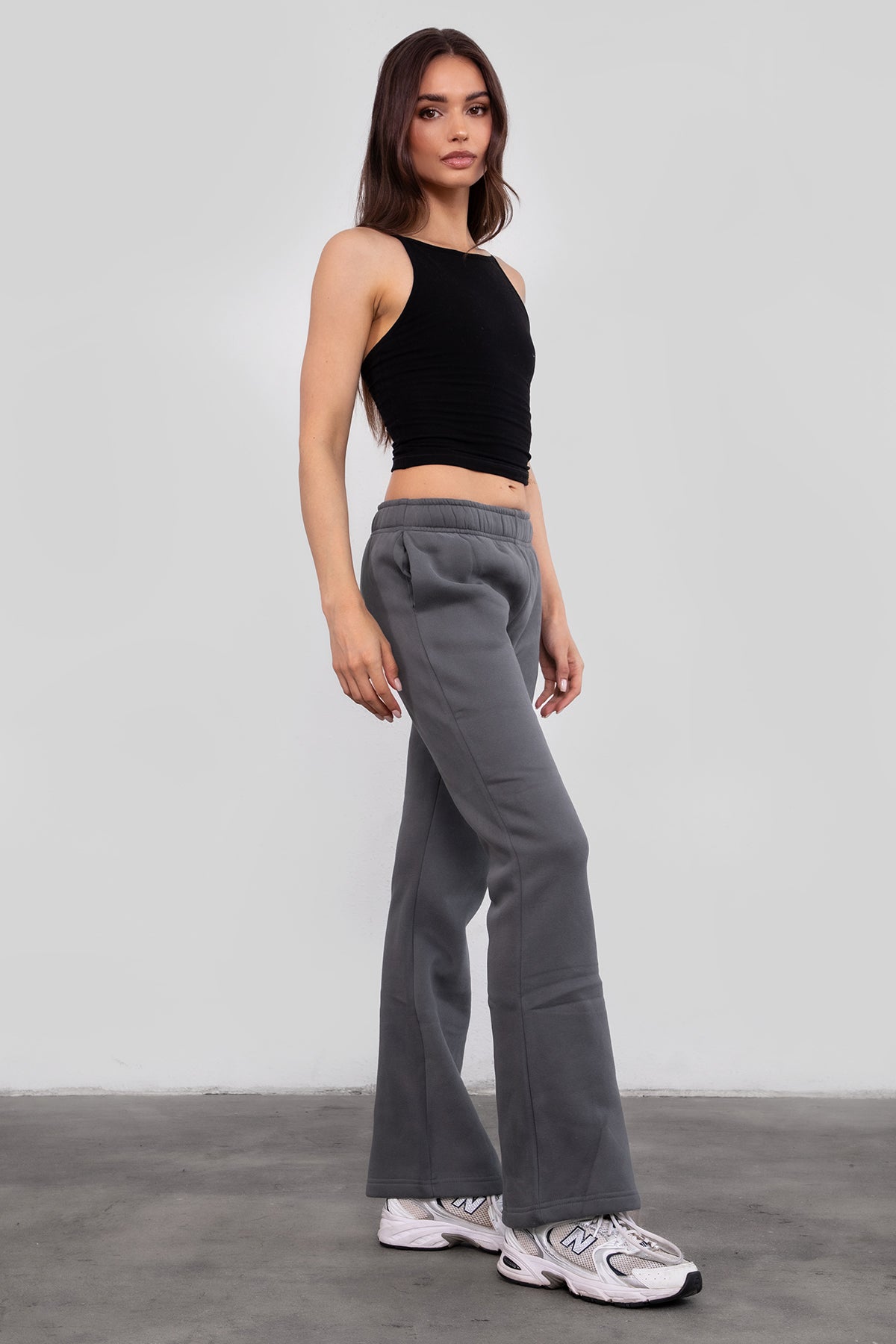 Woman wearing TIC TOC PH29142 JIYA essential fleece flare sweatpants with mid-rise waistband and side pockets from plush fleece collection  in graphite paired with a black cami top. 