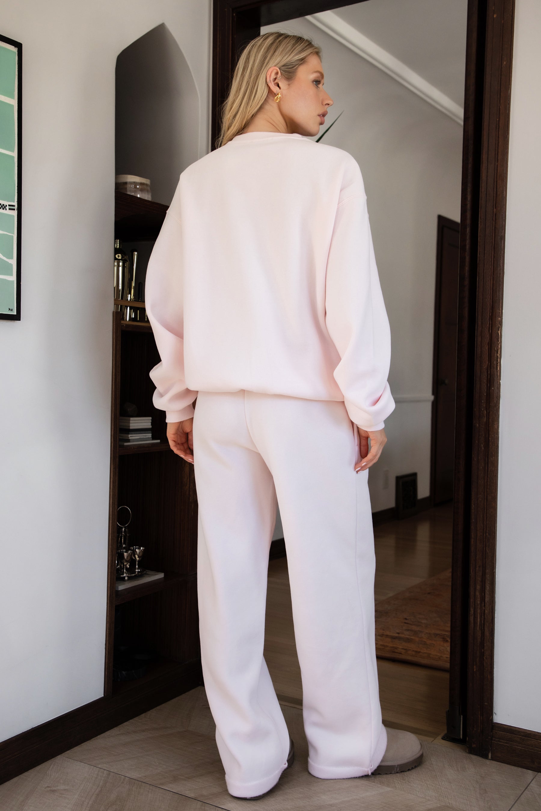 Person wearing a light pink sweater and pants with beige slippers indoors.