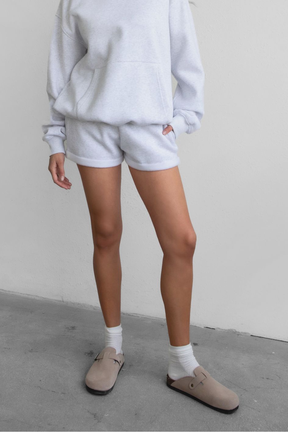 Woman wearing the TIC TOC PJ31004 CARLY ash cloud fleece low rise shorts featuring an elastic waistband with drawcord, deep side pockets, and raw cut hemline with a matching hoodie
