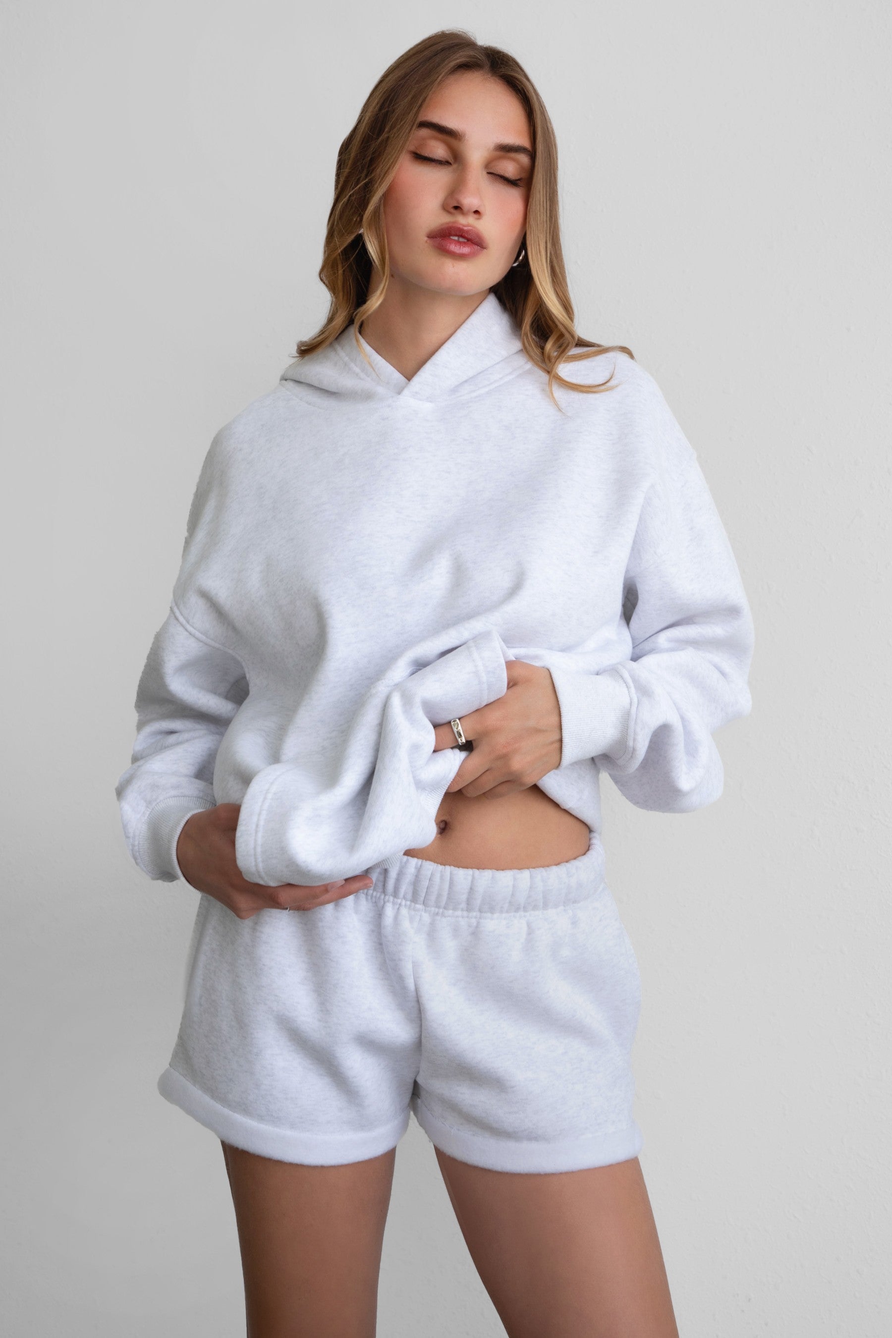 Woman wearing the TIC TOC PJ31004 CARLY ash cloud fleece low rise shorts featuring an elastic waistband with drawcord, deep side pockets, and raw cut hemline with a matching hoodie