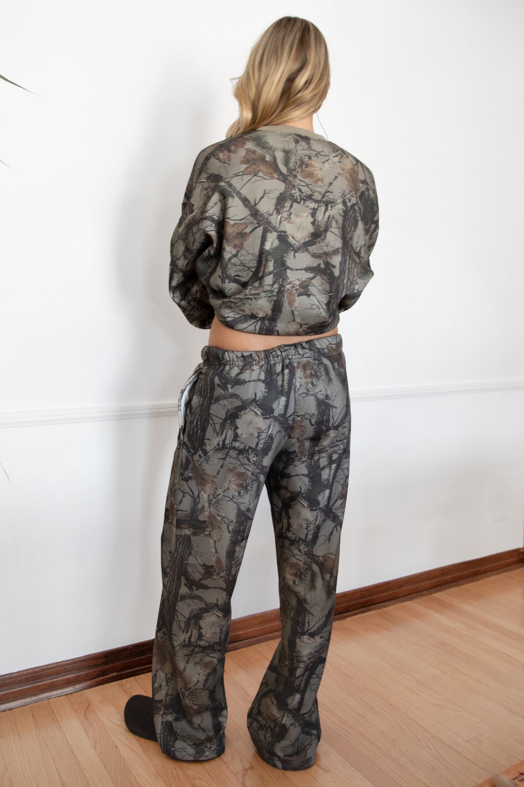 Person wearing a camouflage outfit standing against a white wall.