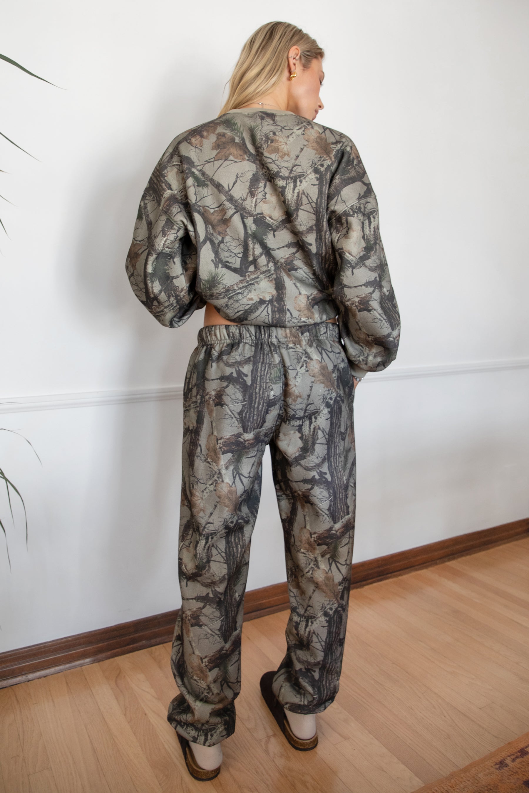 Person wearing a camouflage outfit standing against a white wall.