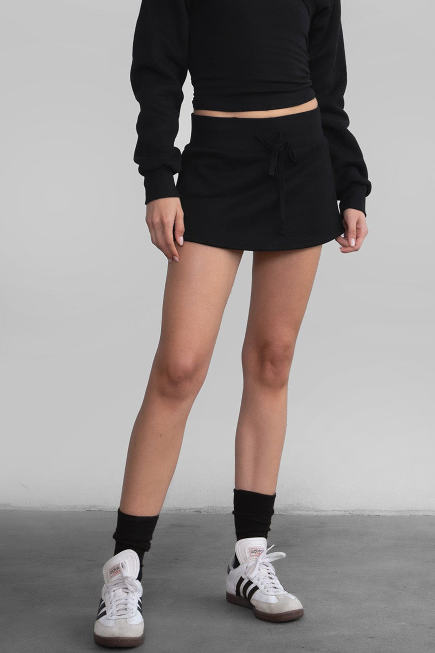 Woman wearing the TIC TOC SH30133BA JEMMA black fleece mini skirt featuring an elastic waistband, drawstring closure, and hidden shorts for comfort and coverage paired with a matching top.