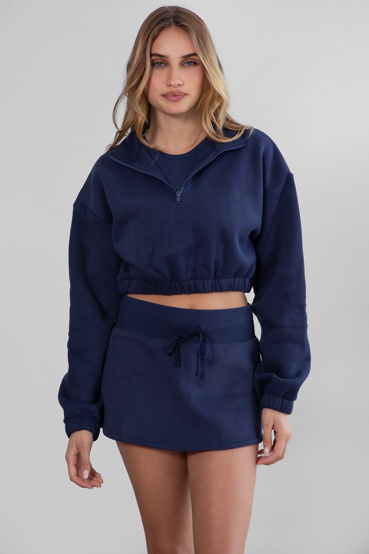 Woman wearing the TIC TOC SH30133BA JEMMA navy fleece mini skirt featuring an elastic waistband, drawstring closure, and hidden shorts for comfort and coverage paired with a matching top.