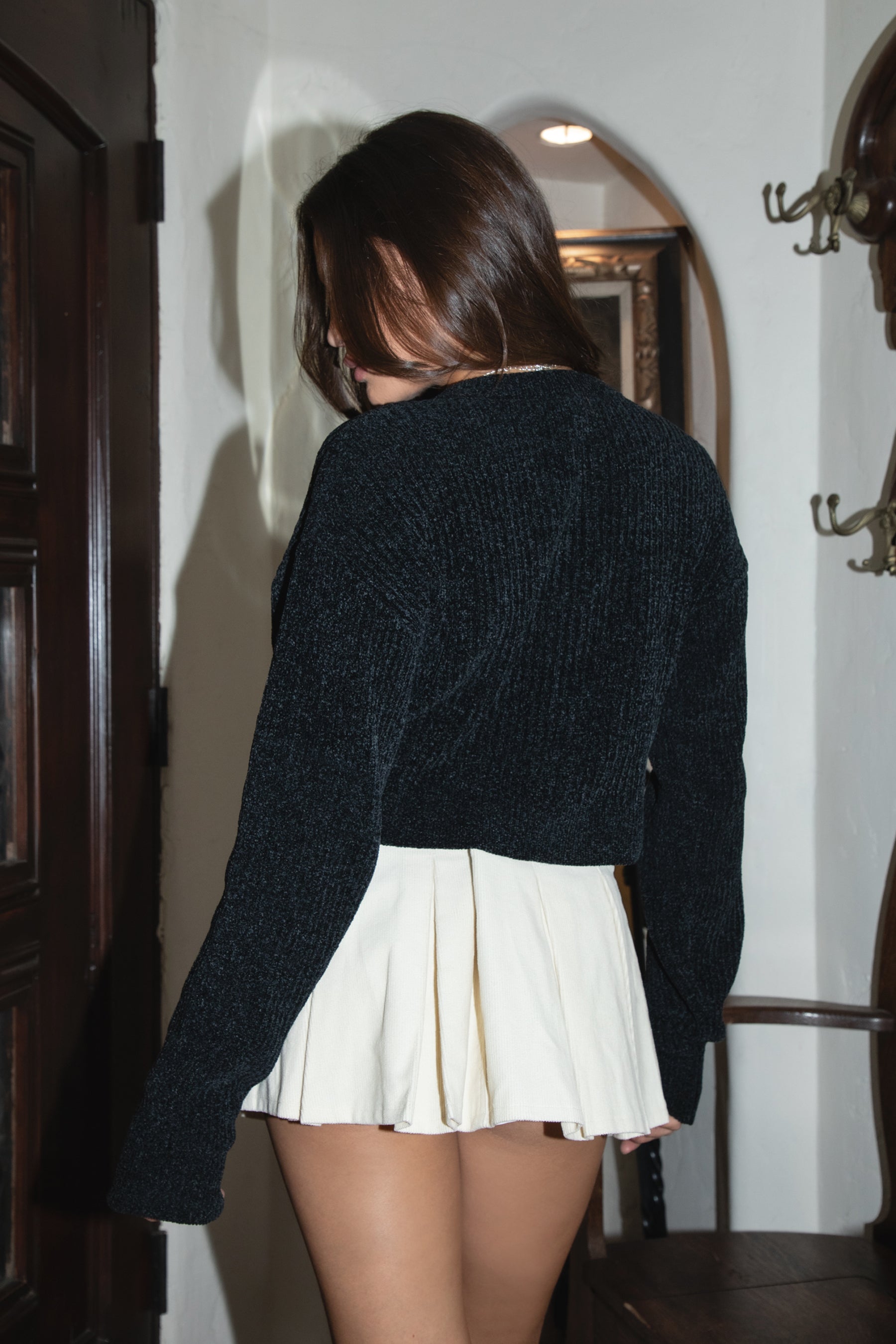 Woman wearing TIC TOC SH31457 BRIDGIA micro corduroy pleated mini skirt with built-in shorts, belt loops, and side zipper with an embroidered black knit cardigan.