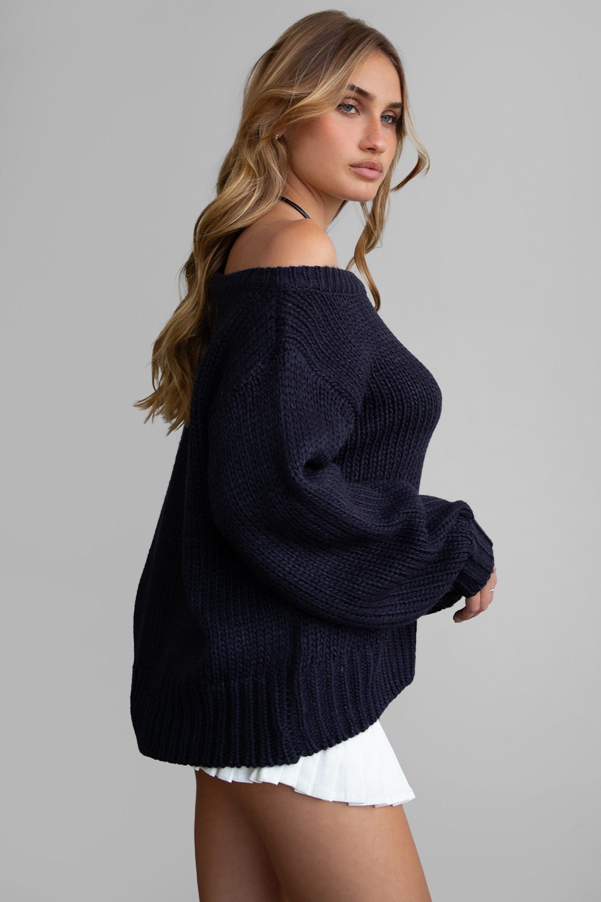 Woman wearing TIC TOC TC30554 BRANDY ribbed knit oversized boat neck off the shoulder sweater in fall casual style with a pleated white mini skirt.