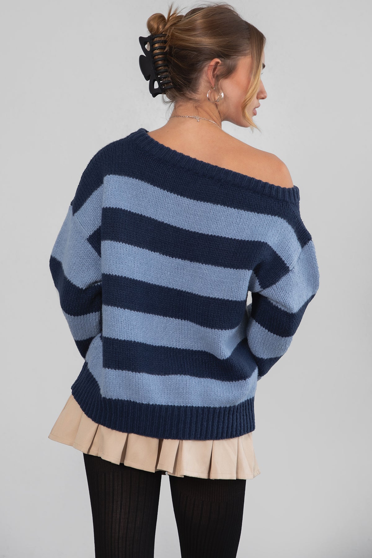 A woman wearing a TIC TOC TC30623 Maddee navy blue rugby knit oversized sweater with an off-the-shoulder neckline and striped color block design, paired with a beige skirt