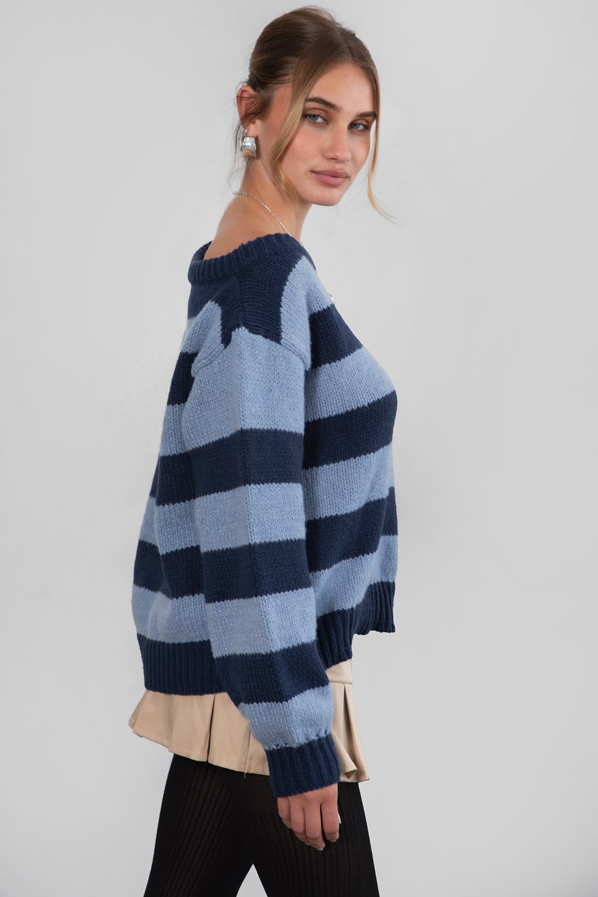 A woman wearing a TIC TOC TC30623 Maddee navy blue rugby knit oversized sweater with an off-the-shoulder neckline and striped color block design, paired with a beige skirt