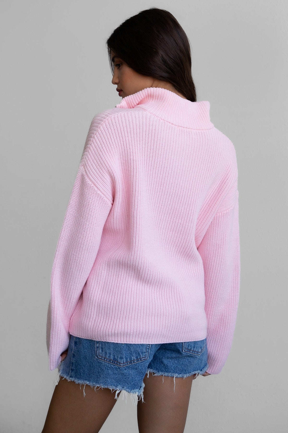 Woman wearing TIC TOC TC30699 LIISA oversized zip sweater with high mock collar and loose bell sleeves in cozy preppy style paired with blue denim shorts. 