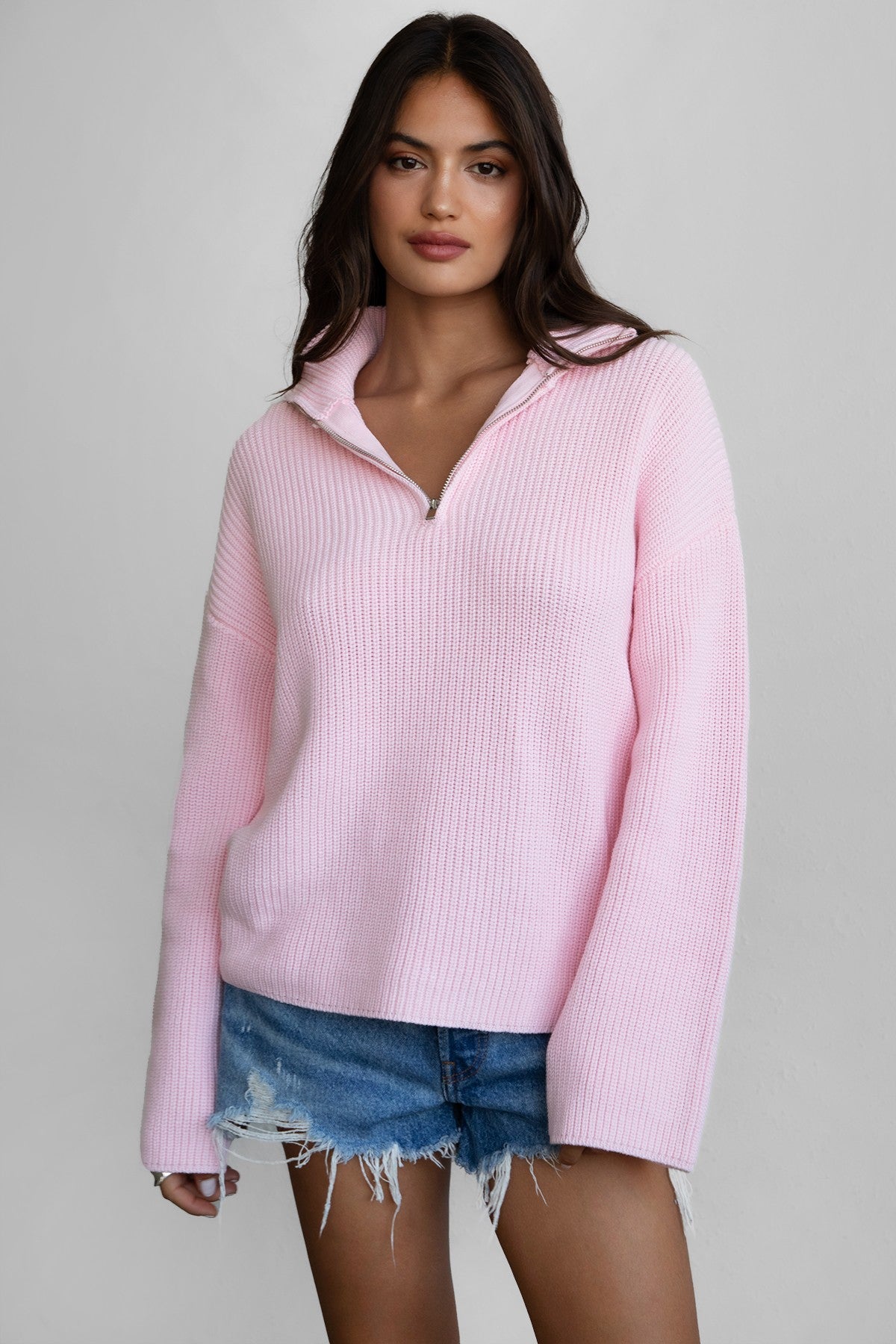 Woman wearing TIC TOC TC30699 LIISA oversized zip sweater with high mock collar and loose bell sleeves in cozy preppy style paired with blue denim shorts. 