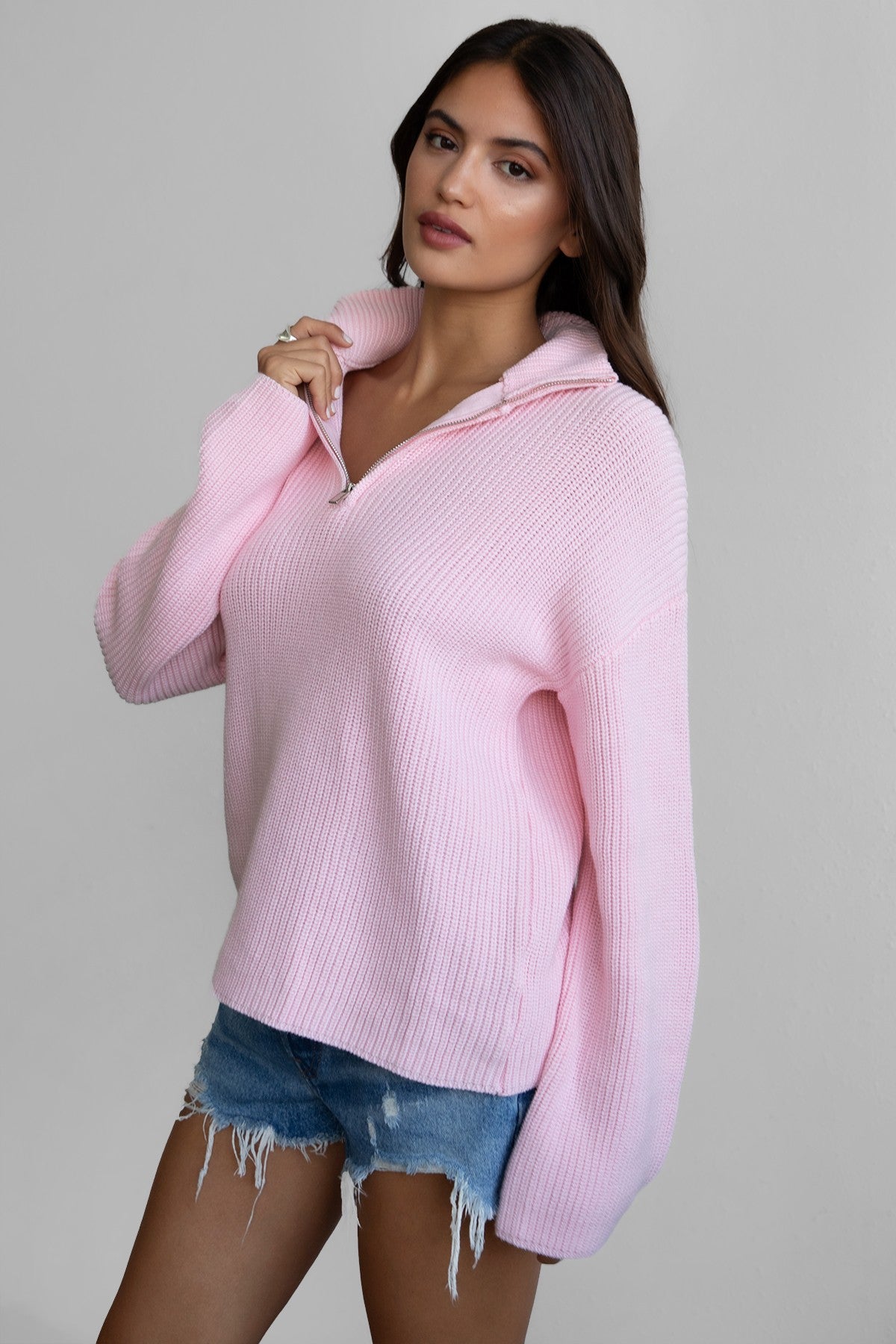 Woman wearing TIC TOC TC30699 LIISA oversized zip sweater with high mock collar and loose bell sleeves in cozy preppy style paired with blue denim shorts. 