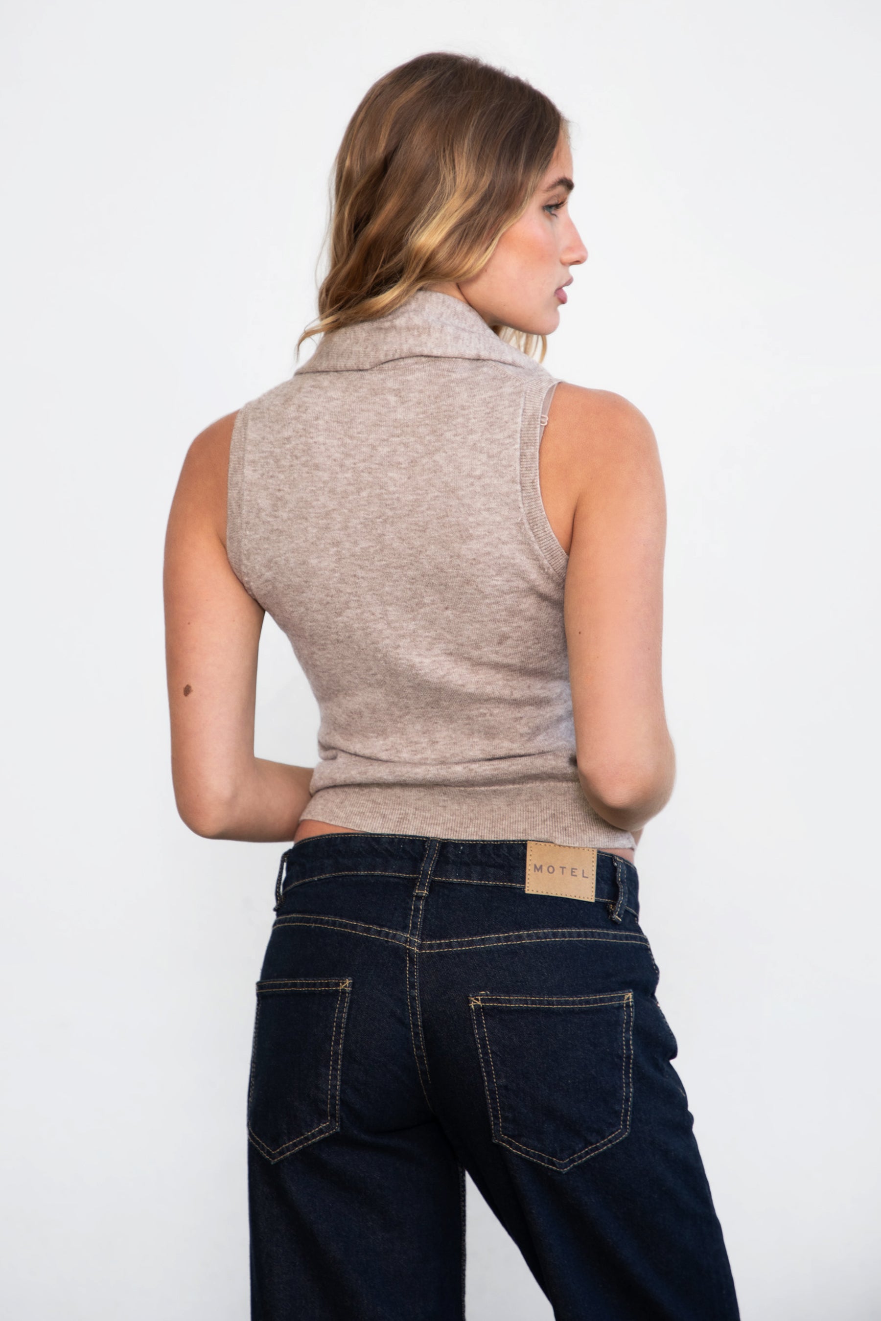 Woman wearing TIC TOC TC31025 BRIGHETTE sleeveless knit sweater with high crew neckline and removable scarf in heather marled brown paired with dark denim pants. 
