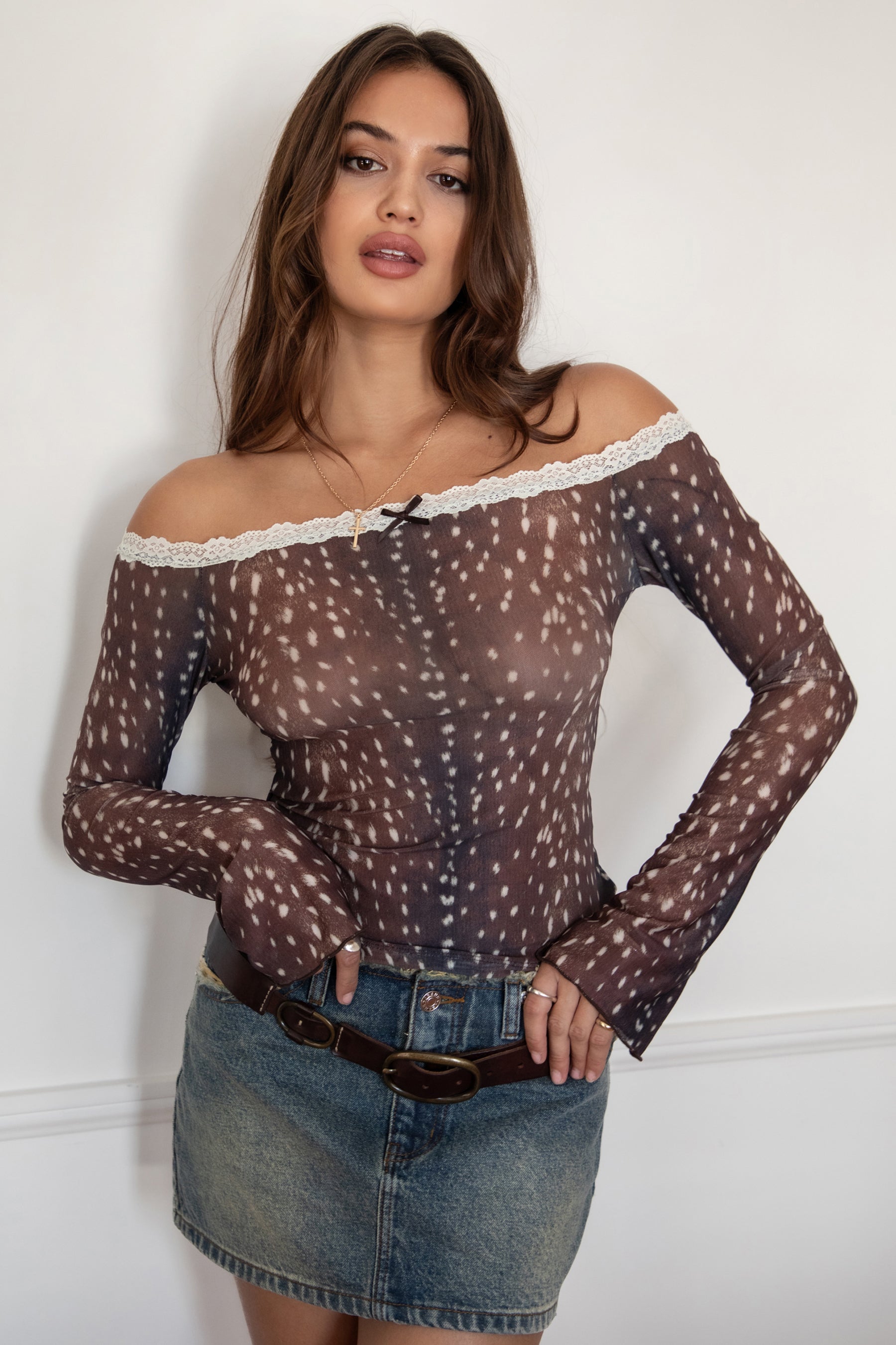 Woman wearing the TIC TOC TC31579 BAMBELLE off-the-shoulder top featuring a deer-inspired mesh print, lace trim neckline, and long bell sleeves paired with a distressed denim mini skirt