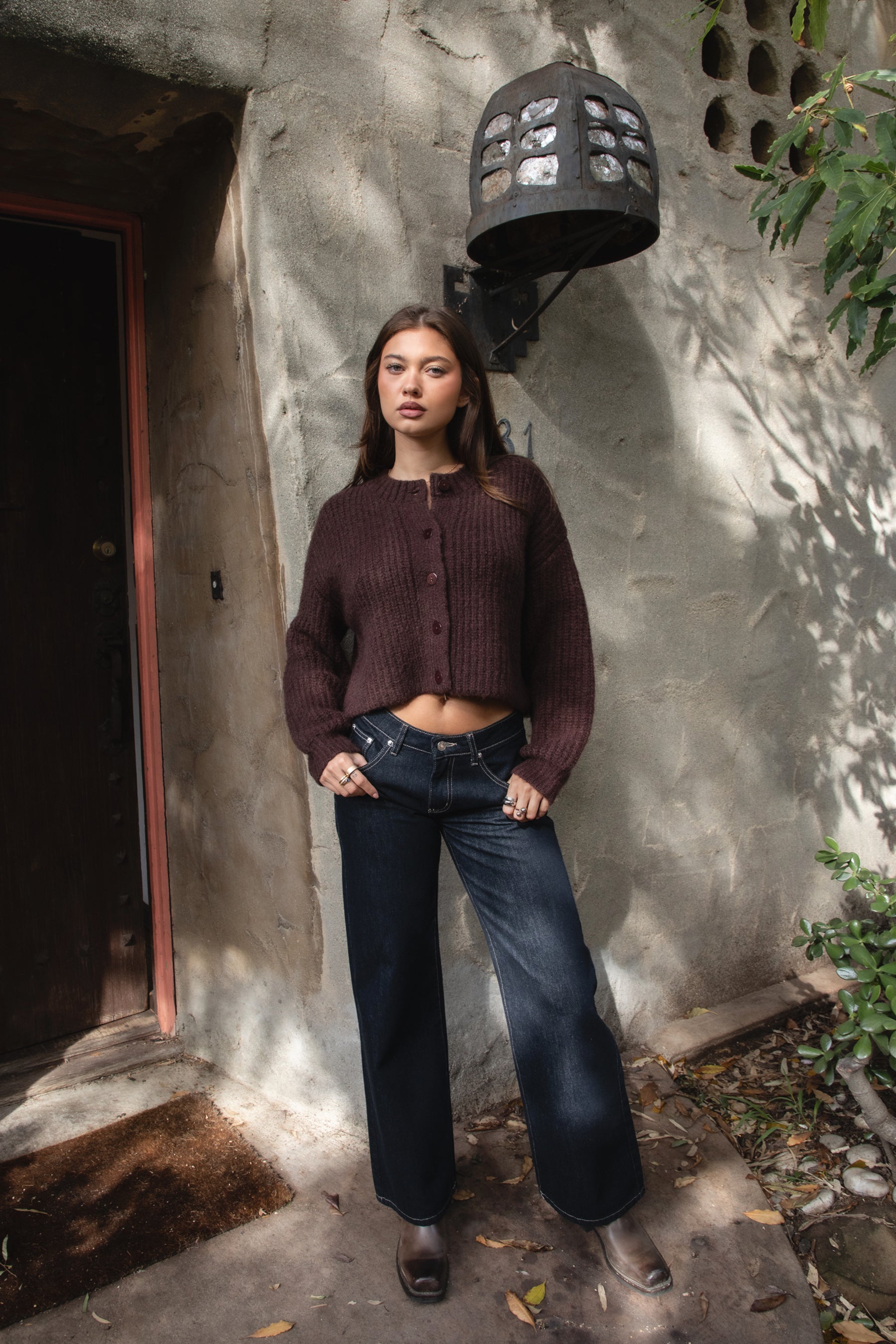 Woman wearing TIC TOC TF31833 ISOLDE brown wool-blend button down cardigan with boxy cropped fit, ribbed trim, and marled knit texture paired with dark jeans and boots against a textured wall.