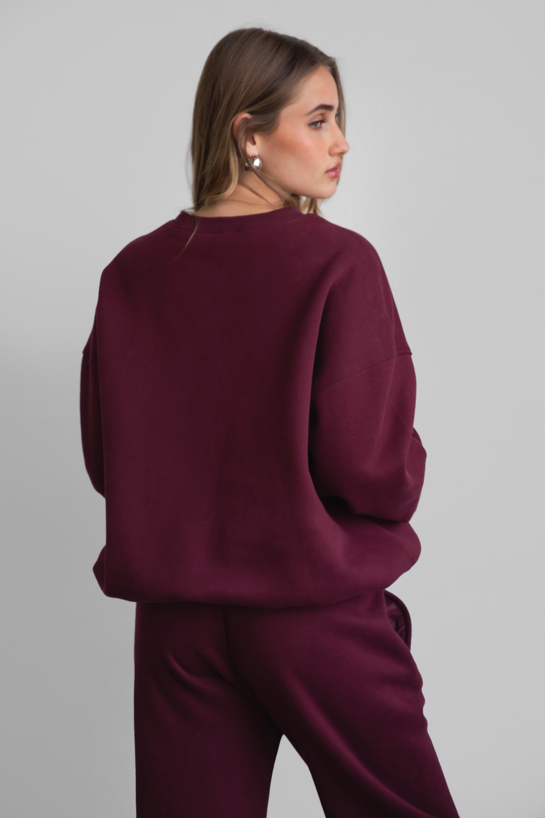 Woman wearing the TIC TOC TH28243 VARSITY black cherry fleece crew neck pullover sweatshirt featuring dropped shoulders, ribbed trim, and plush fleece fabric with the matching bottoms 