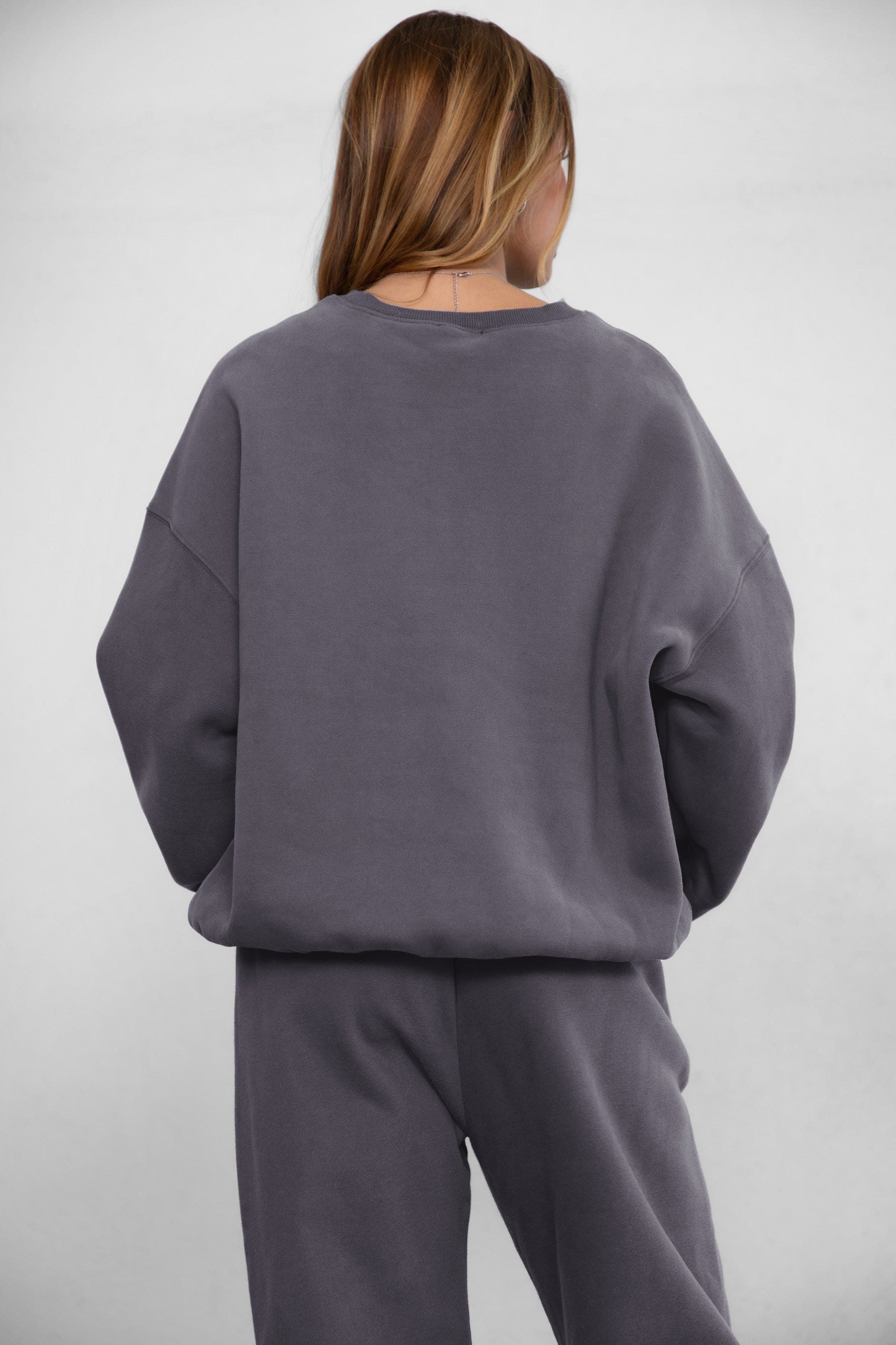 Woman wearing the TIC TOC TH28243 VARSITY charcoal fleece crew neck pullover sweatshirt featuring dropped shoulders, ribbed trim, and plush fleece fabric with the matching bottoms 