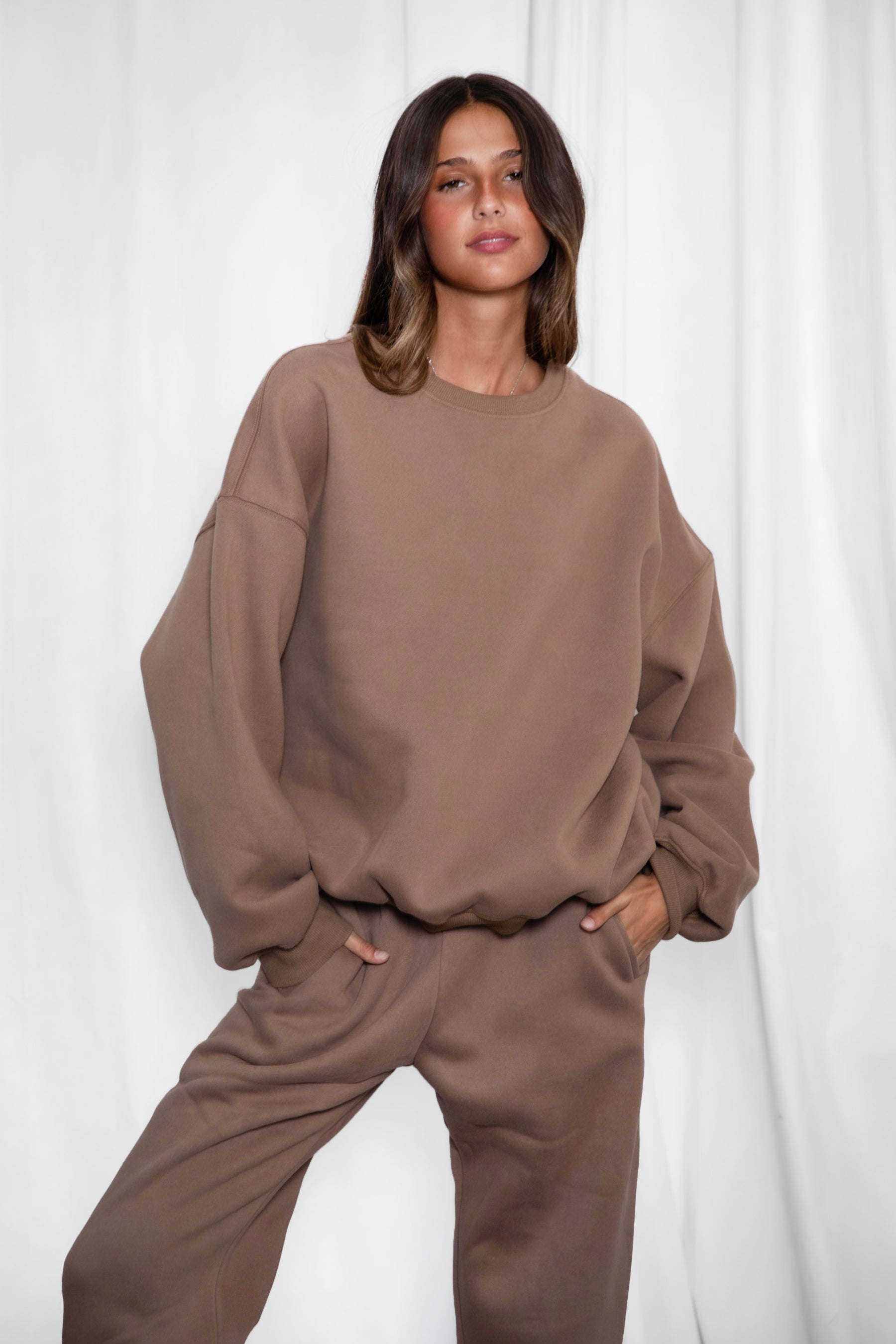 Woman wearing the TIC TOC TH28243 VARSITY coffee fleece crew neck pullover sweatshirt featuring dropped shoulders, ribbed trim, and plush fleece fabric with the matching bottoms 