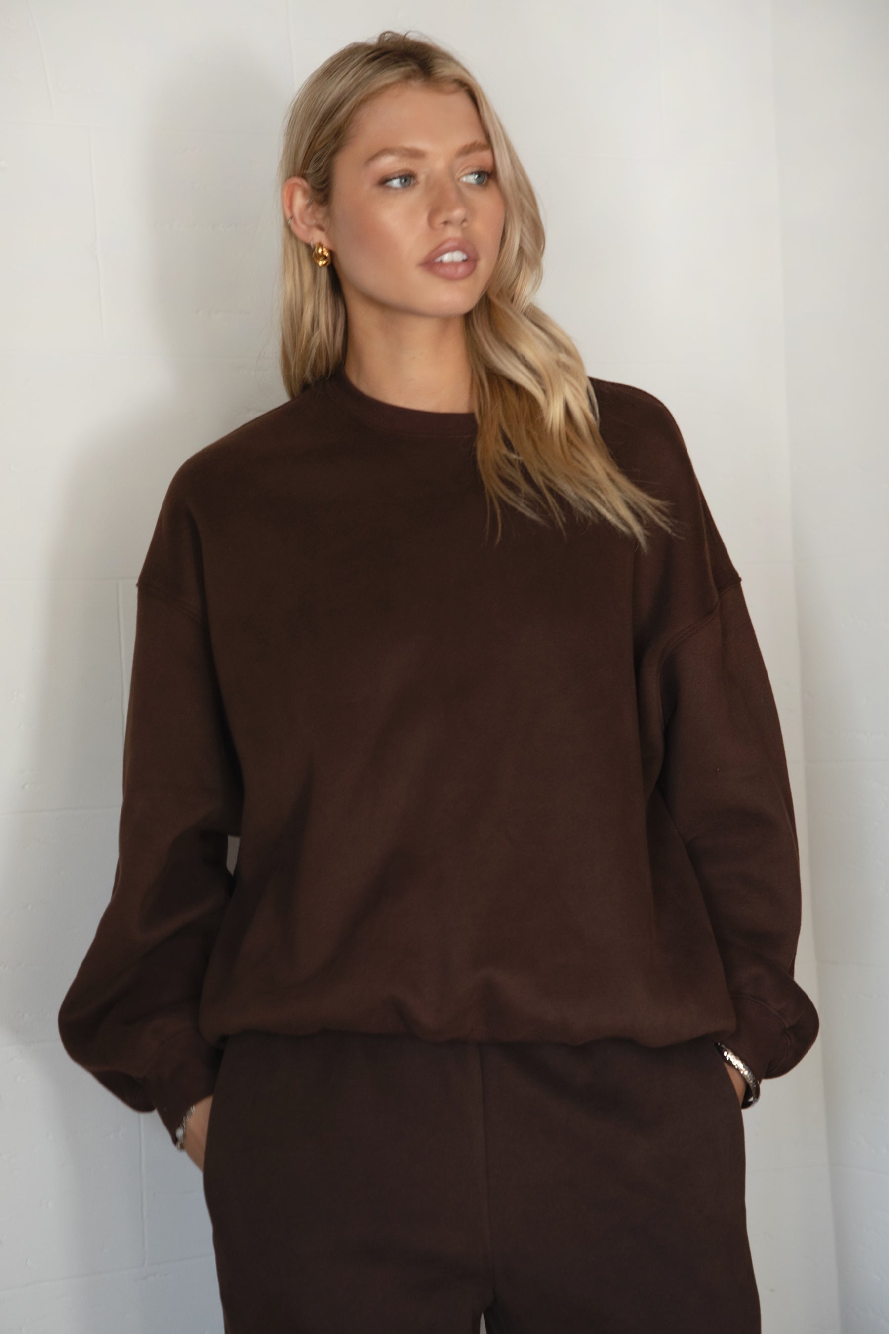 Woman wearing the TIC TOC TH28243 VARSITY brown fleece crew neck pullover sweatshirt featuring dropped shoulders, ribbed trim, and plush fleece fabric with the matching bottoms 