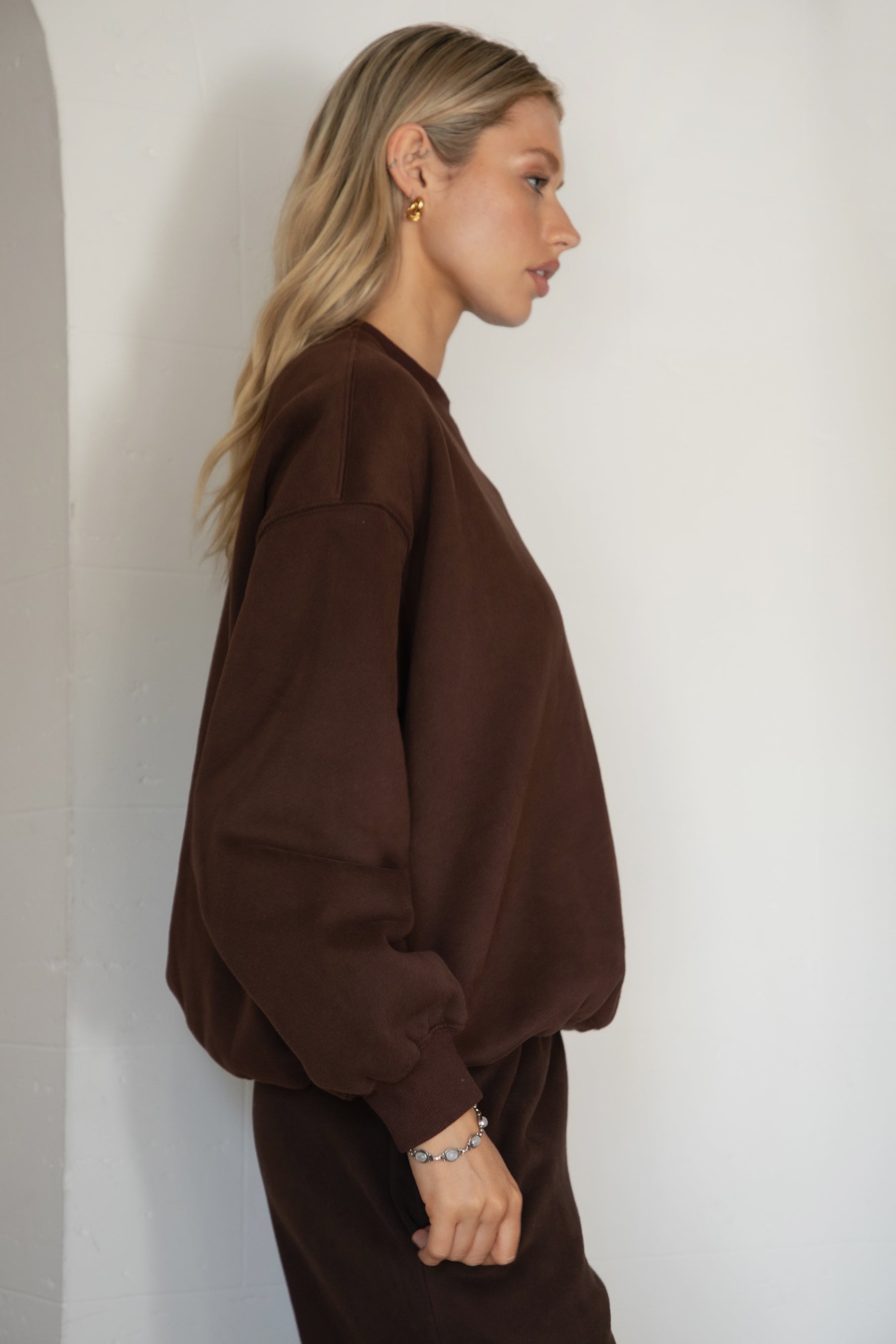 Woman wearing the TIC TOC TH28243 VARSITY brown fleece crew neck pullover sweatshirt featuring dropped shoulders, ribbed trim, and plush fleece fabric with the matching bottoms 