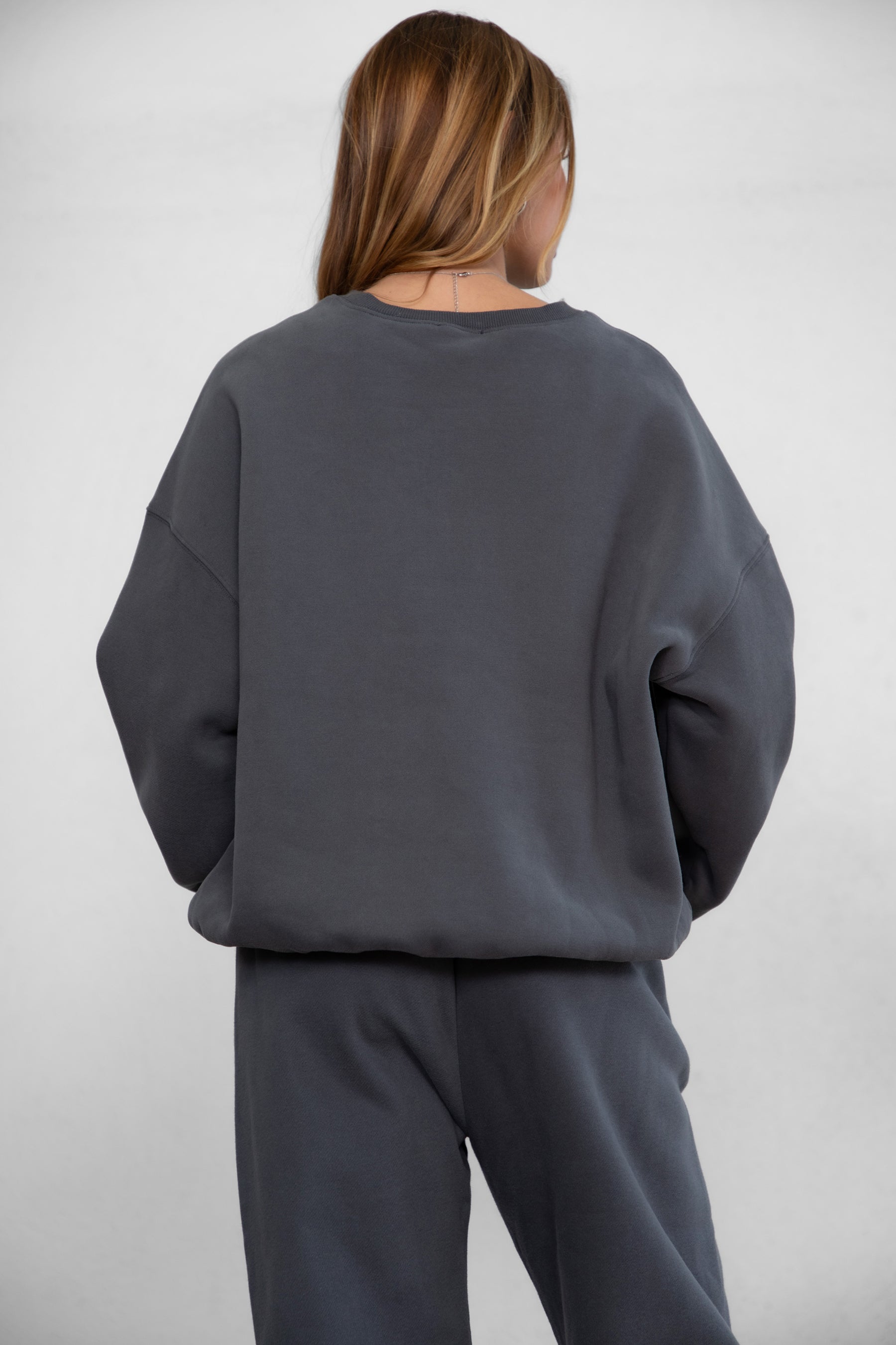Woman wearing the TIC TOC TH28243 VARSITY graphite fleece crew neck pullover sweatshirt featuring dropped shoulders, ribbed trim, and plush fleece fabric with the matching bottoms 