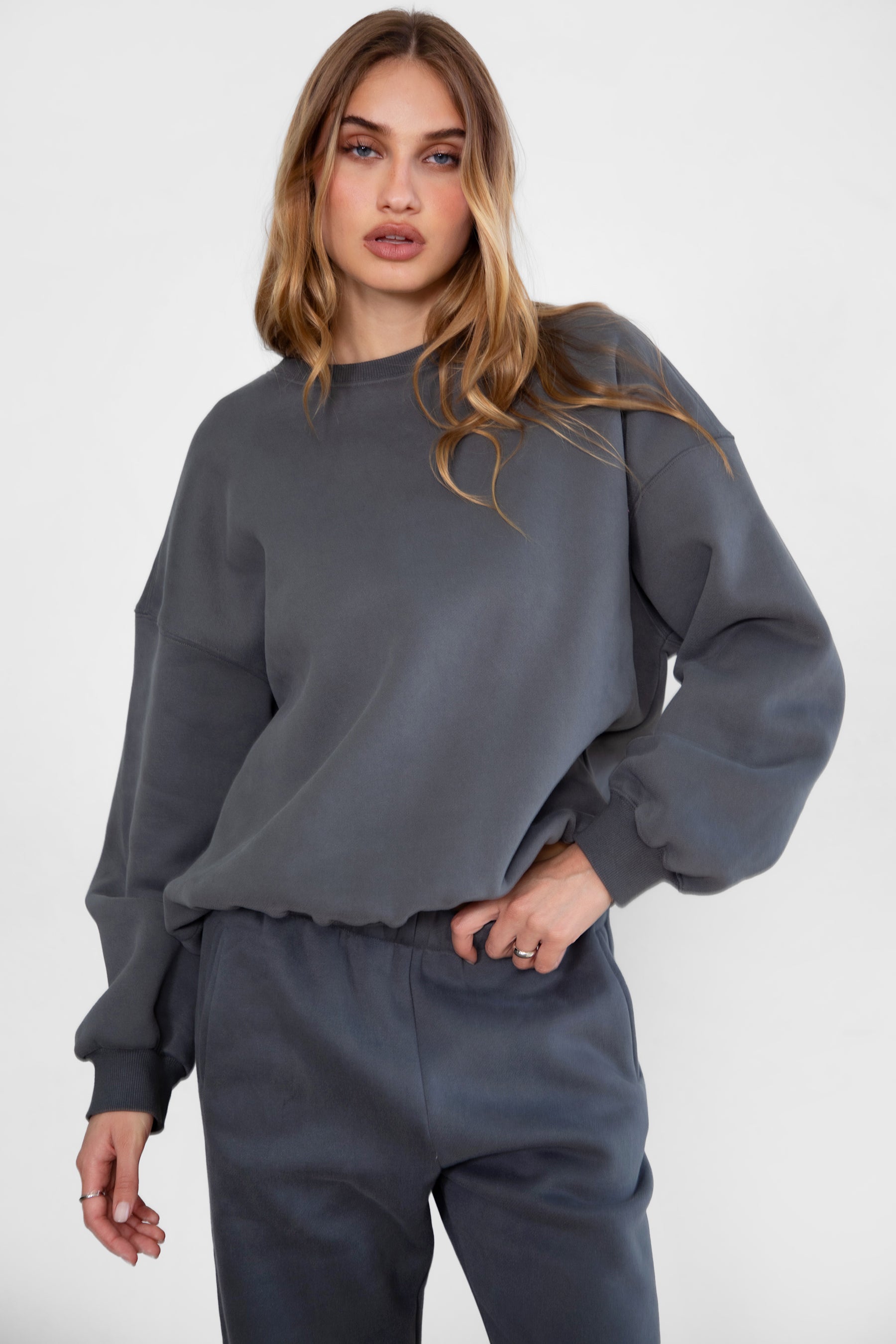 Woman wearing the TIC TOC TH28243 VARSITY graphite fleece crew neck pullover sweatshirt featuring dropped shoulders, ribbed trim, and plush fleece fabric with the matching bottoms 
