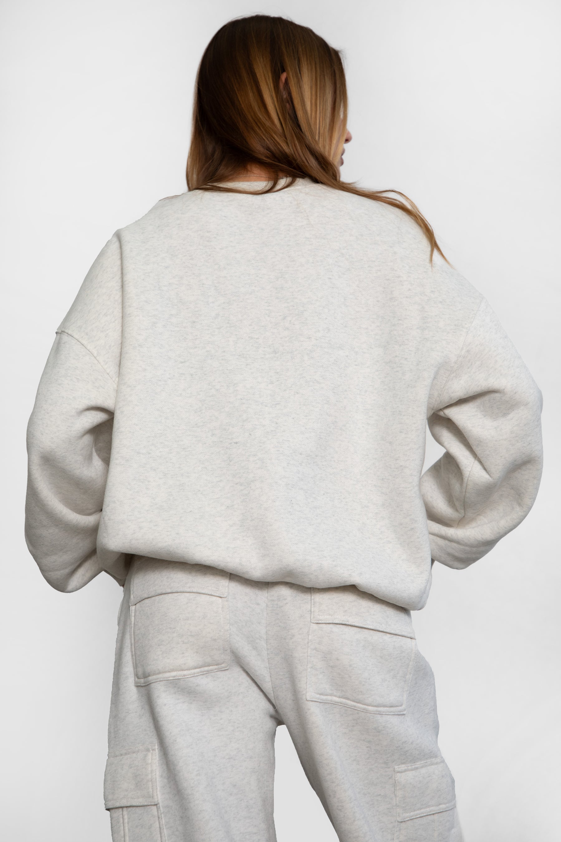 Woman wearing the TIC TOC TH28243 VARSITY heather white fleece crew neck pullover sweatshirt featuring dropped shoulders, ribbed trim, and plush fleece fabric with the matching bottoms 