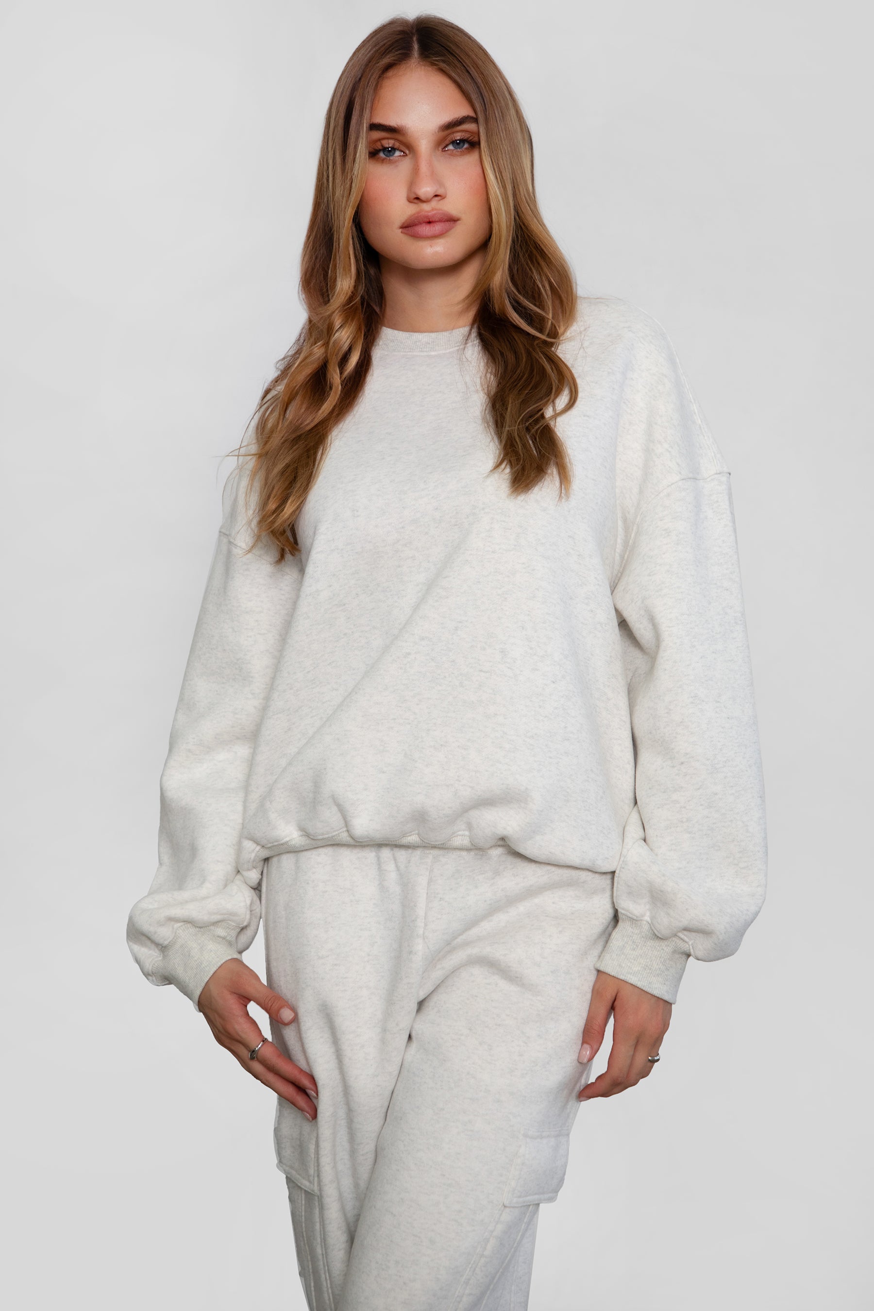 Woman wearing the TIC TOC TH28243 VARSITY heather white fleece crew neck pullover sweatshirt featuring dropped shoulders, ribbed trim, and plush fleece fabric with the matching bottoms 