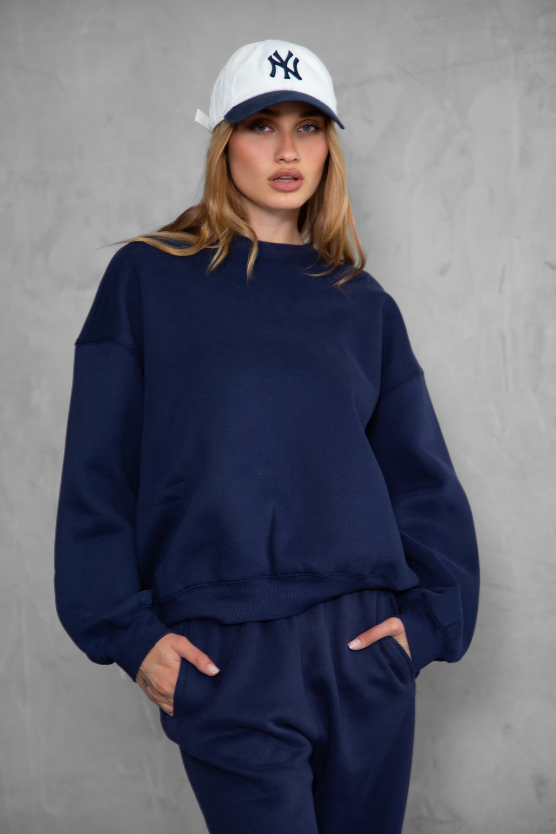 Woman wearing the TIC TOC TH28243 VARSITY navy blue fleece crew neck pullover sweatshirt featuring dropped shoulders, ribbed trim, and plush fleece fabric with the matching bottoms 