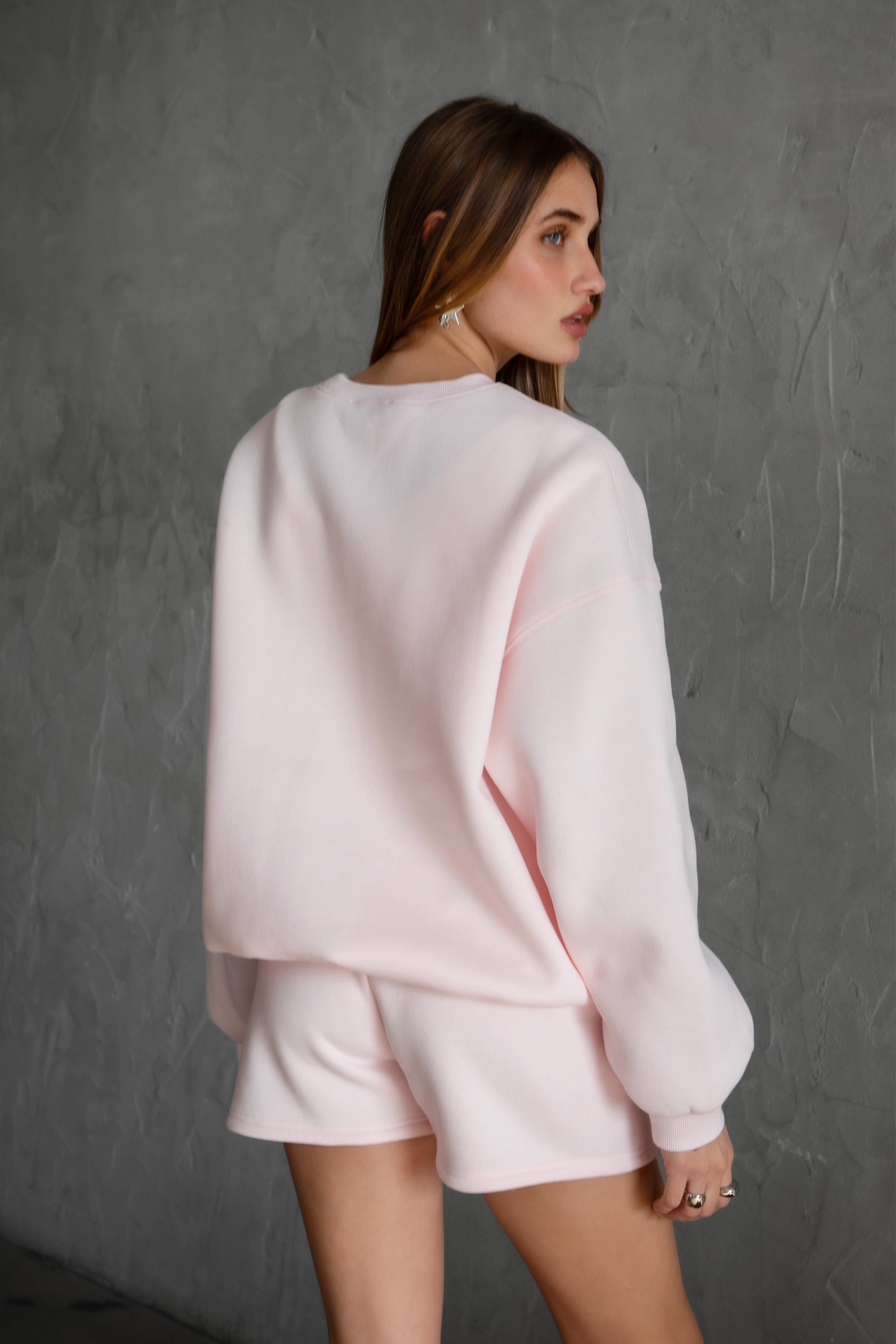 Woman wearing the TIC TOC TH28243 VARSITY pale pink fleece crew neck pullover sweatshirt featuring dropped shoulders, ribbed trim, and plush fleece fabric with the matching bottoms 