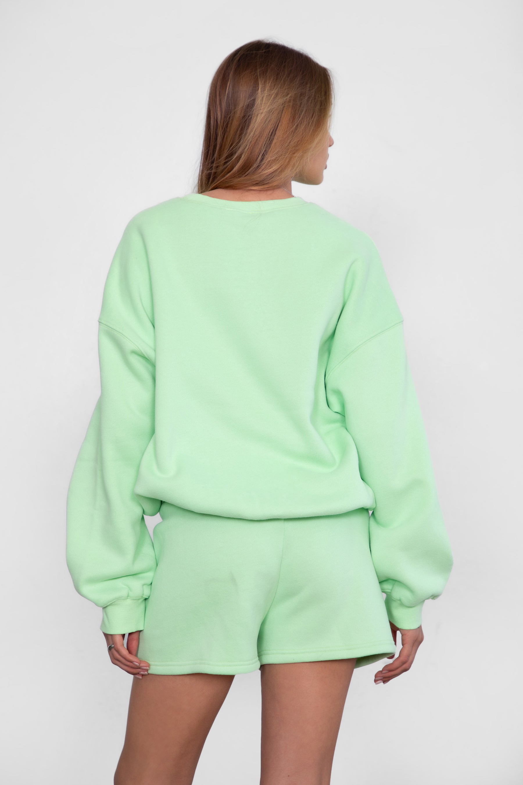 Woman wearing the TIC TOC TH28243 VARSITY pastel lime fleece crew neck pullover sweatshirt featuring dropped shoulders, ribbed trim, and plush fleece fabric with the matching bottoms 