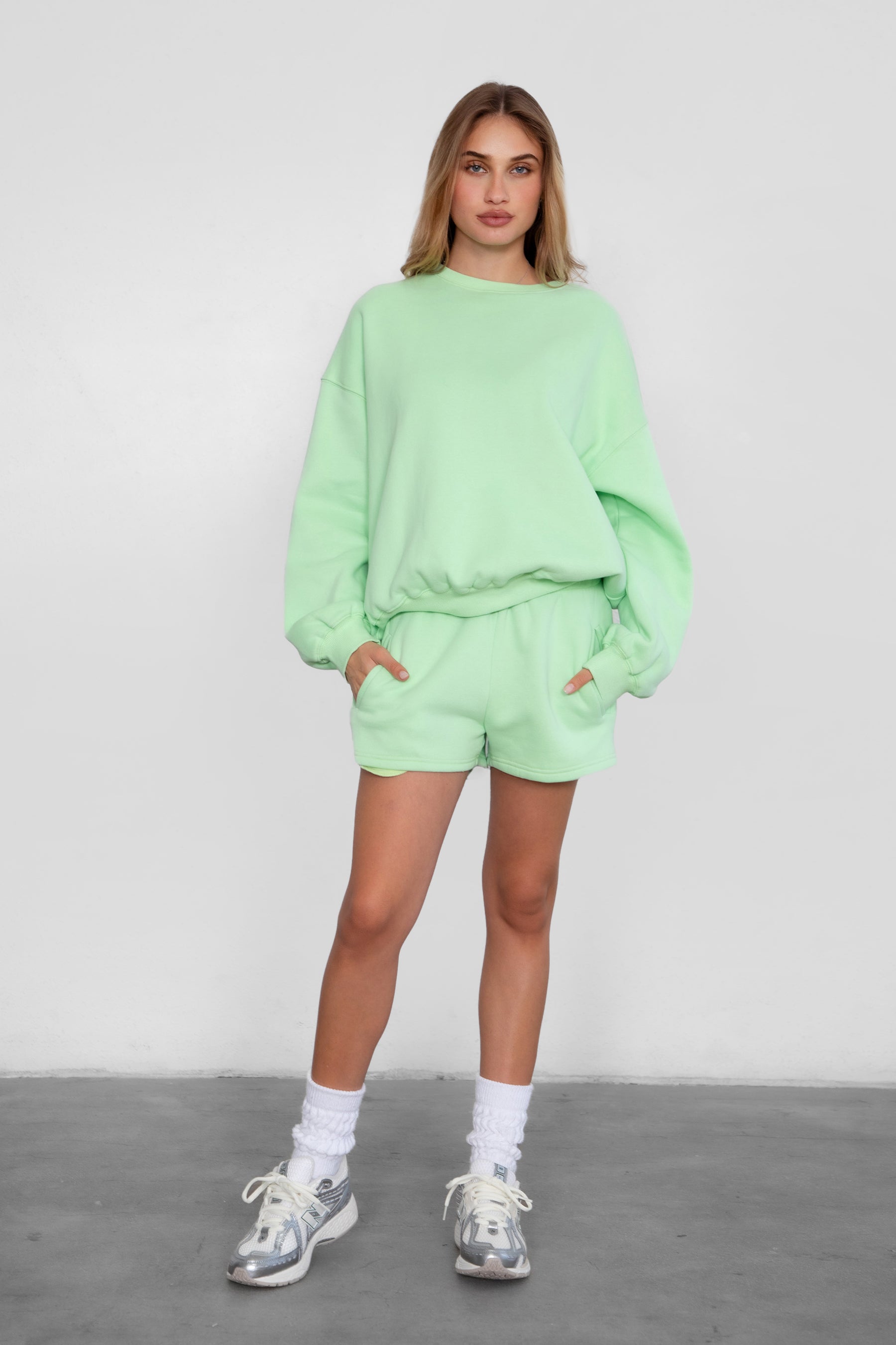 Woman wearing the TIC TOC TH28243 VARSITY pastel lime fleece crew neck pullover sweatshirt featuring dropped shoulders, ribbed trim, and plush fleece fabric with the matching bottoms 